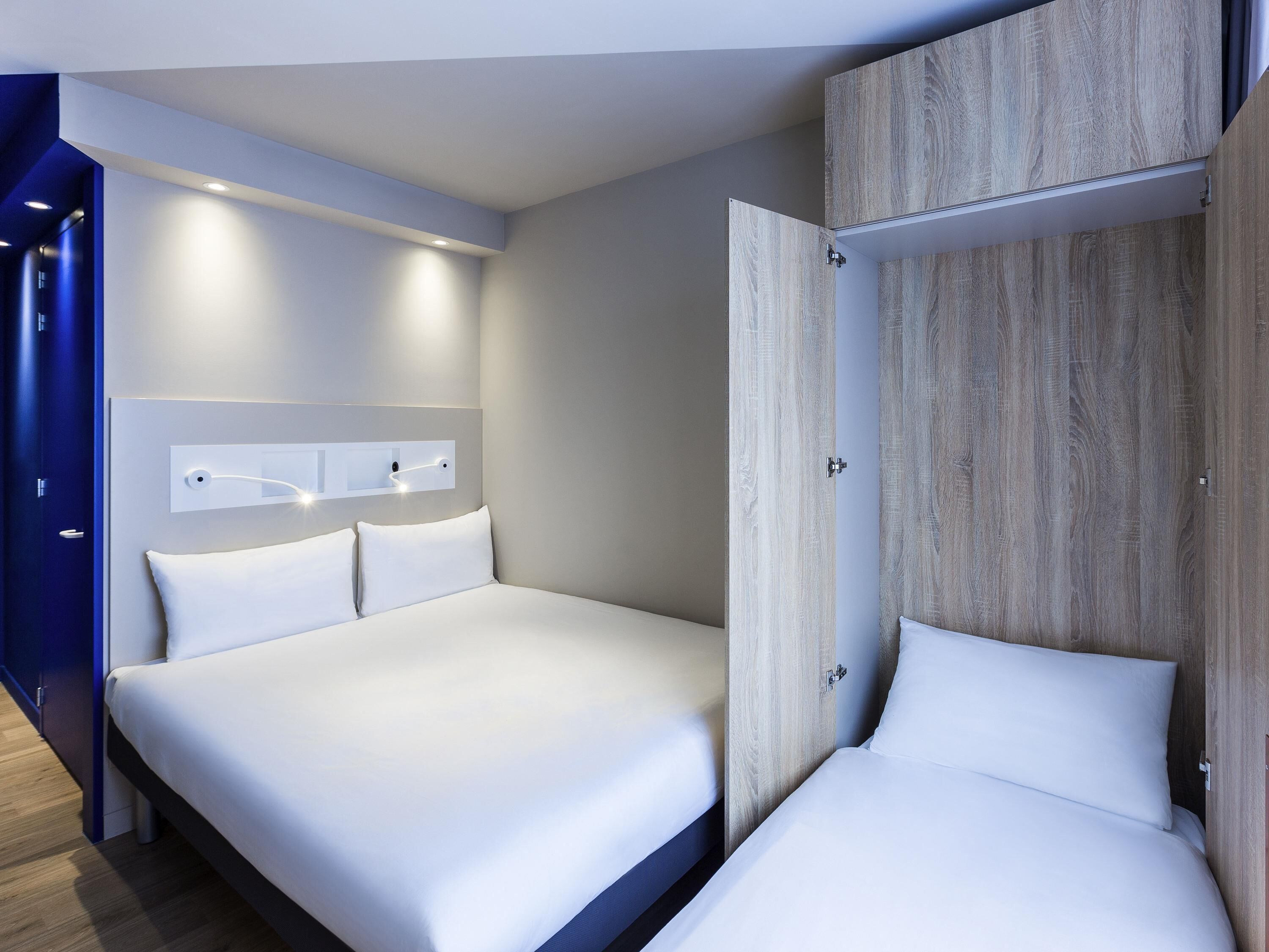 Una habitación de hotel moderna con una cama grande, un armario y una lámpara fijada a la pared.