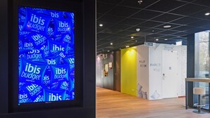 Een moderne hotelgang met een digitaal scherm waarop herhaaldelijk het woord 'ibis' staat.