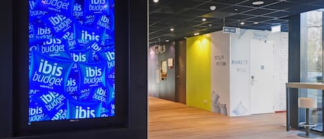 A modern hotel corridor with a digital display featuring the word "ibis" repeatedly.