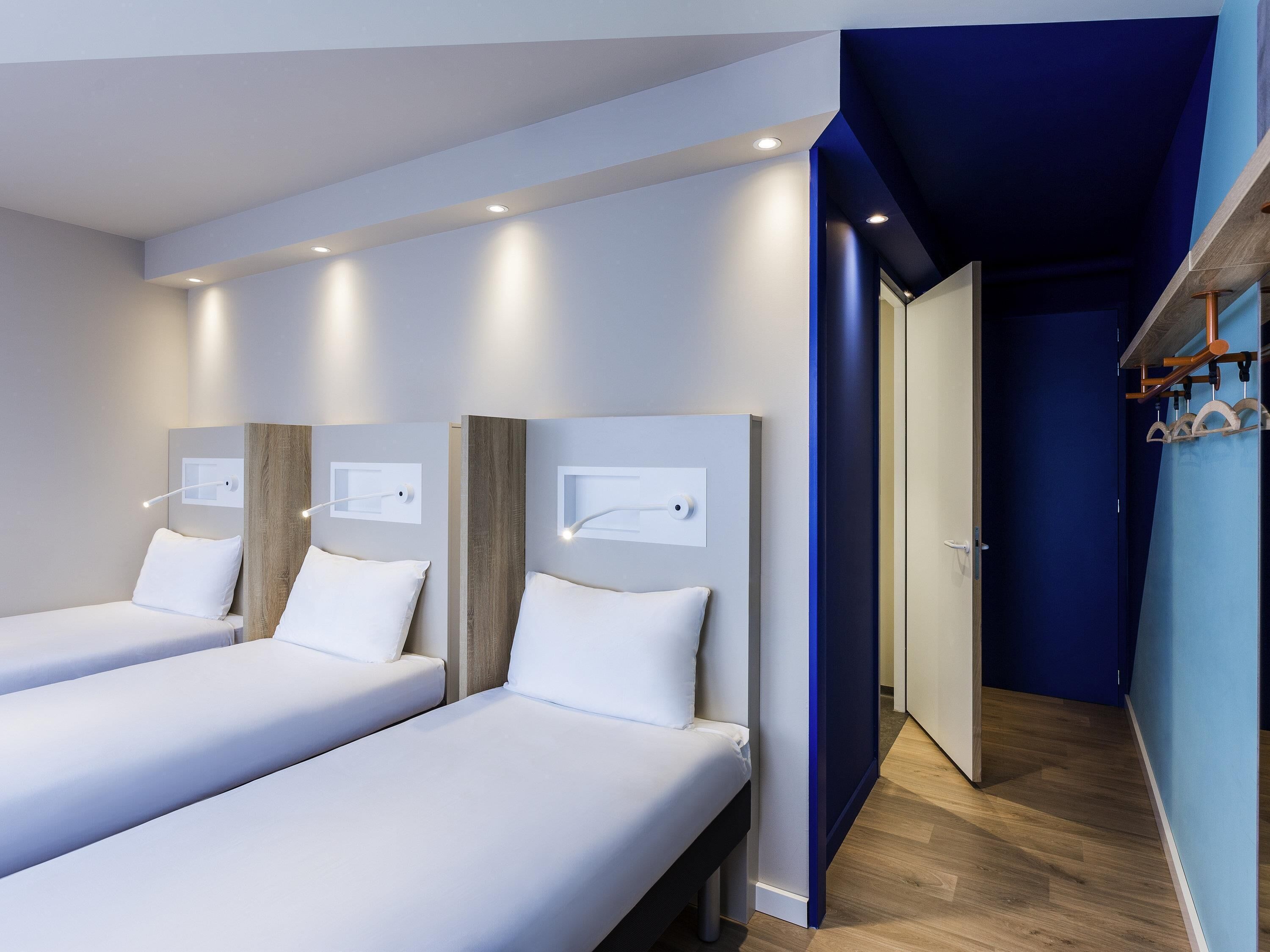 Habitación de hotel con dos camas, cabecero de madera, pared decorada en azul y piso de madera.