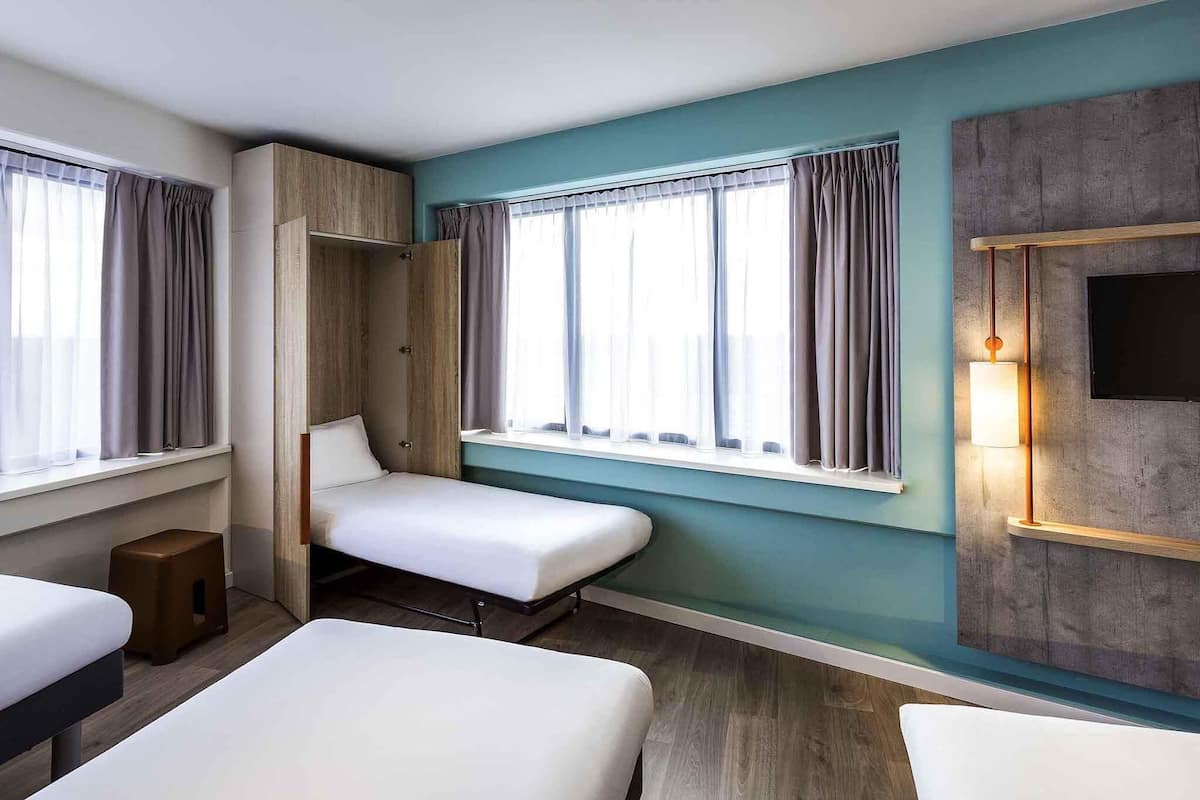 A hotel room with two beds, a wardrobe, a small stool, and a TV mounted on the wall.