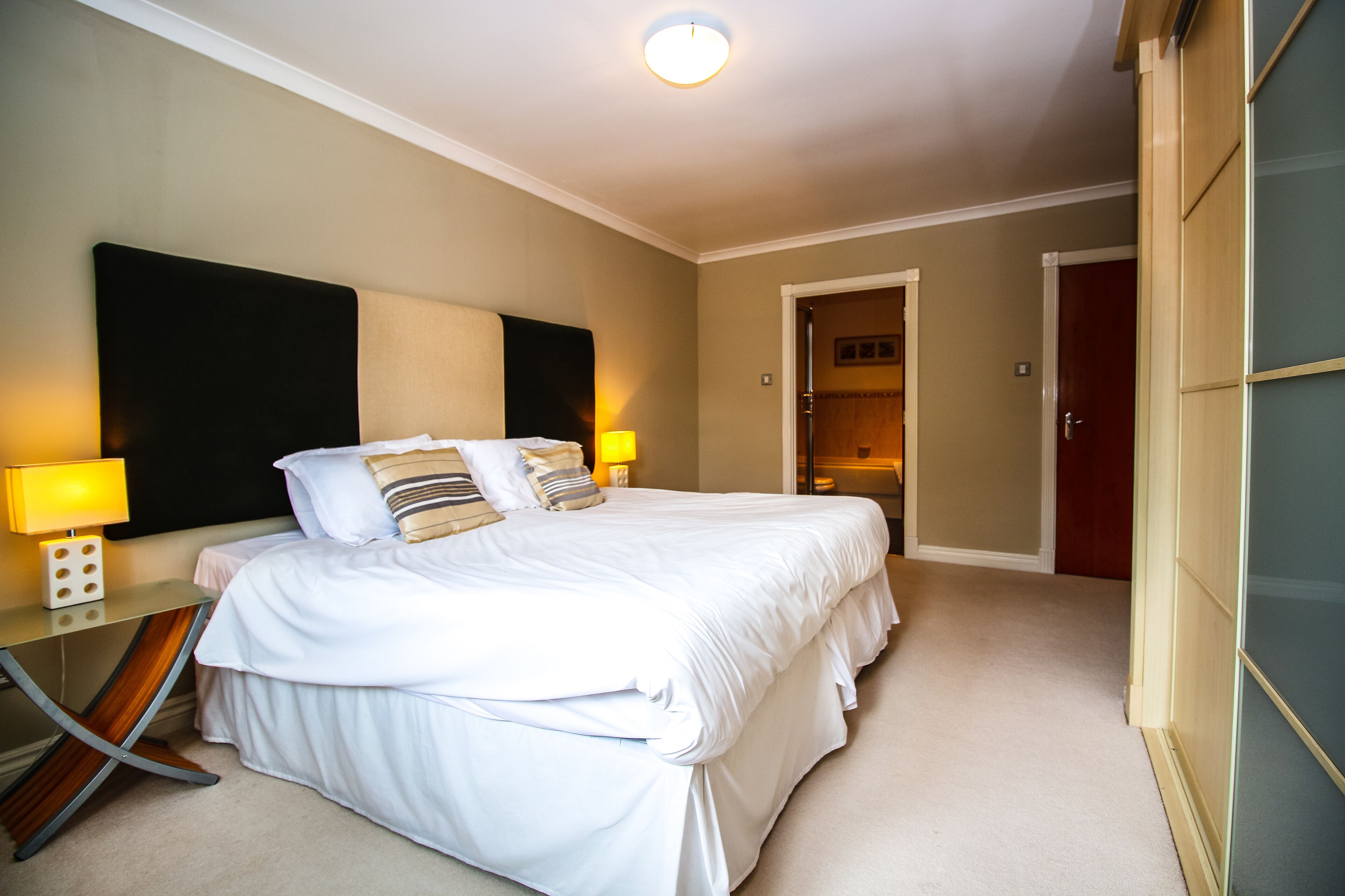 A neatly arranged bedroom with a large bed, bedside lamps, a wardrobe, and a door leading to a closet.