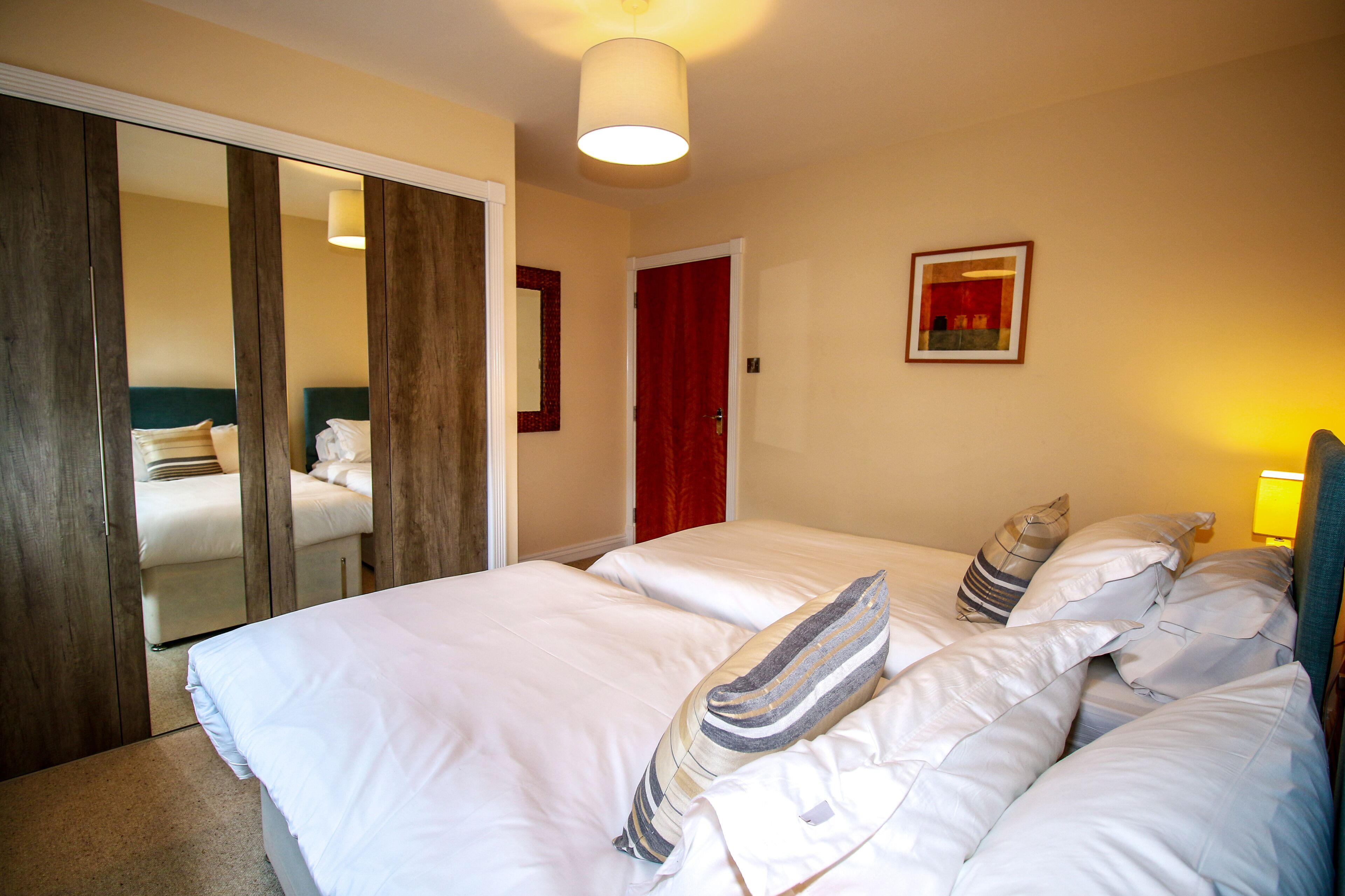 A hotel room with a large bed, a wardrobe, a mirror, and a red door.