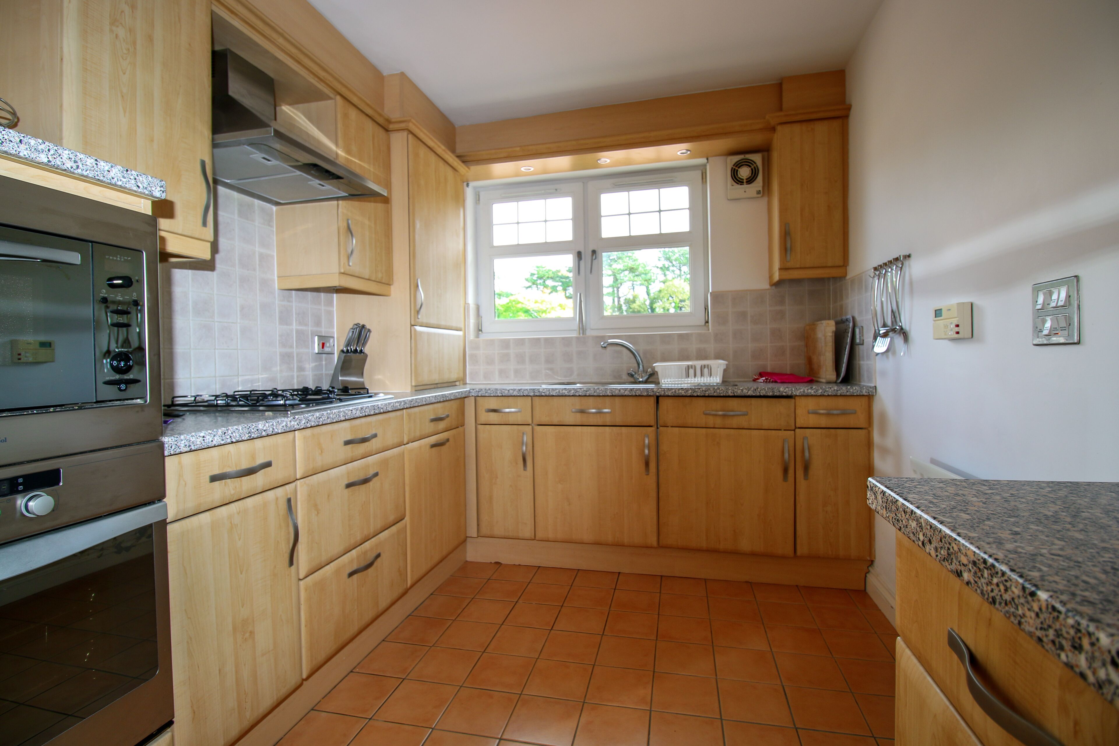 A kitchen with wooden cabinets, a stainless steel stove, and a window with a view of greenery outside.