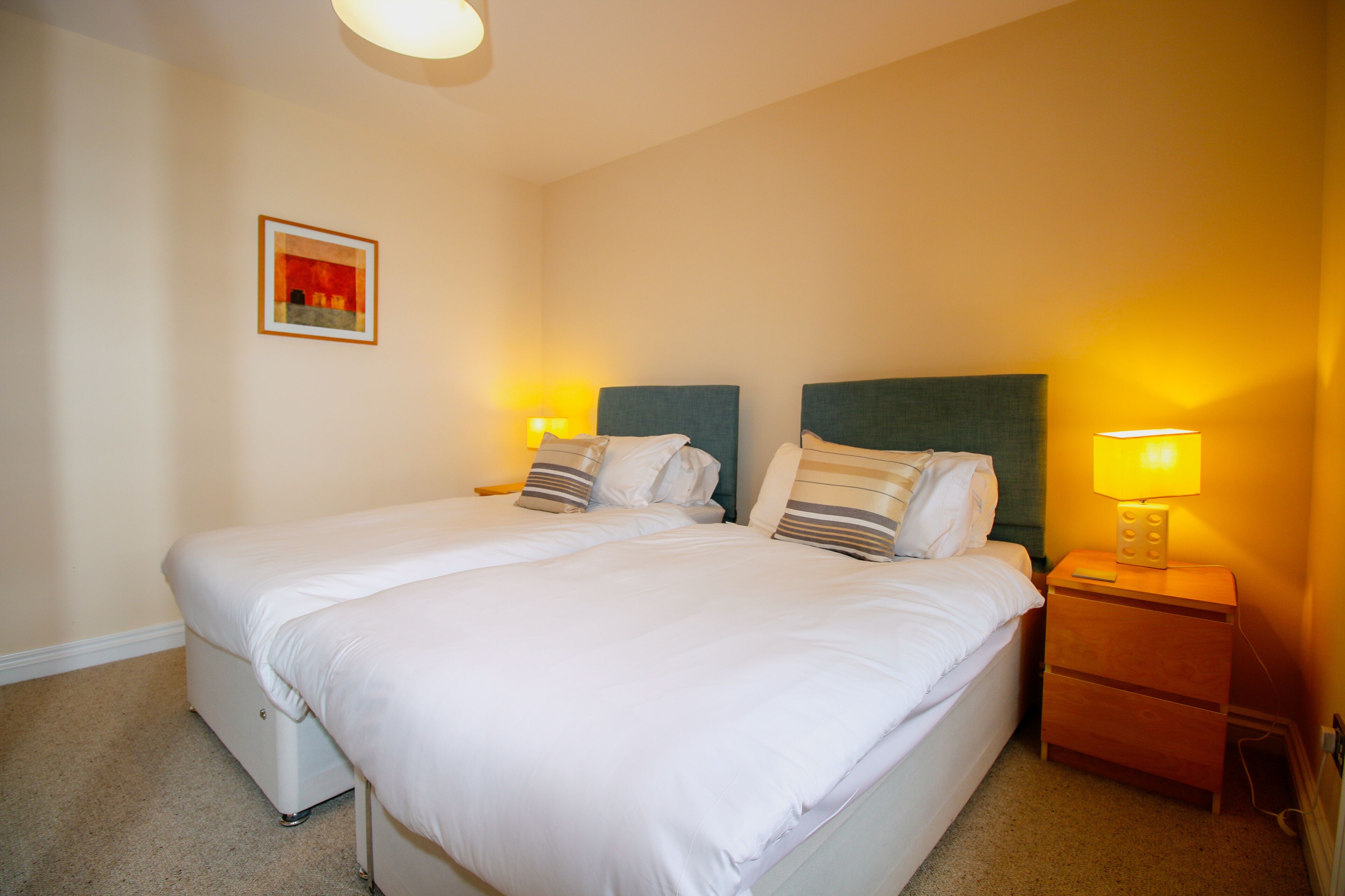A double bed with white bedding, two bedside tables with lamps, and a framed picture on the wall.