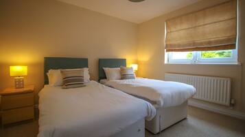 A bedroom with two single beds, bedside tables with lamps, a window with a blind, and a radiator.