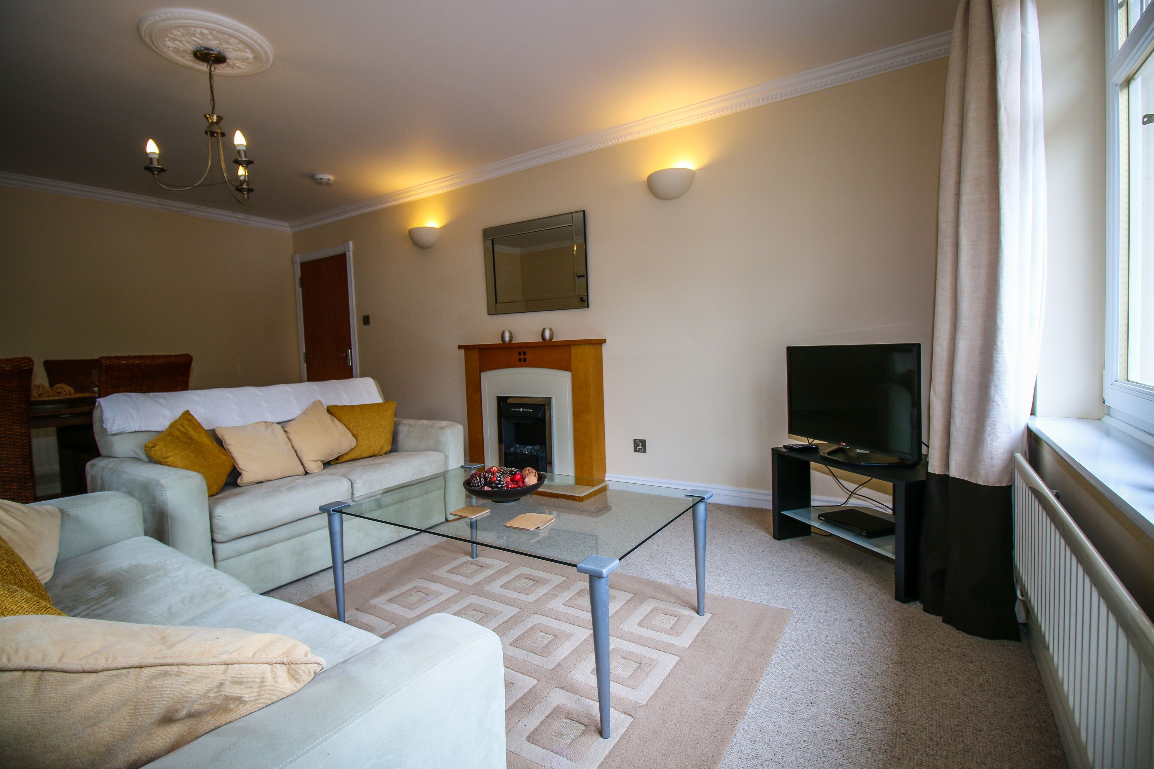 A living room with a glass coffee table, a sofa, a fireplace, and a television.