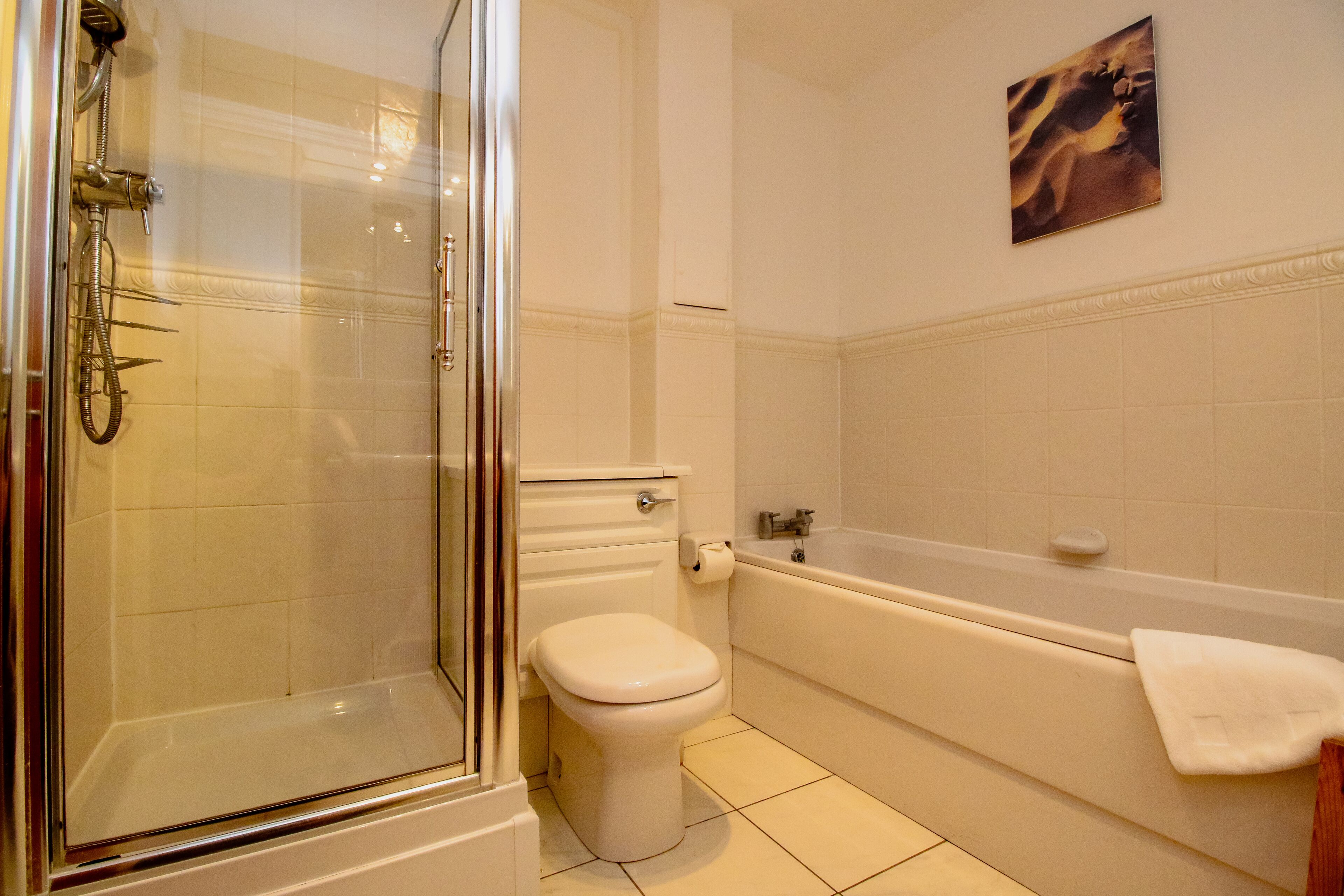 A bathroom with a glass-enclosed shower, a toilet, and a bathtub with a towel on the edge.