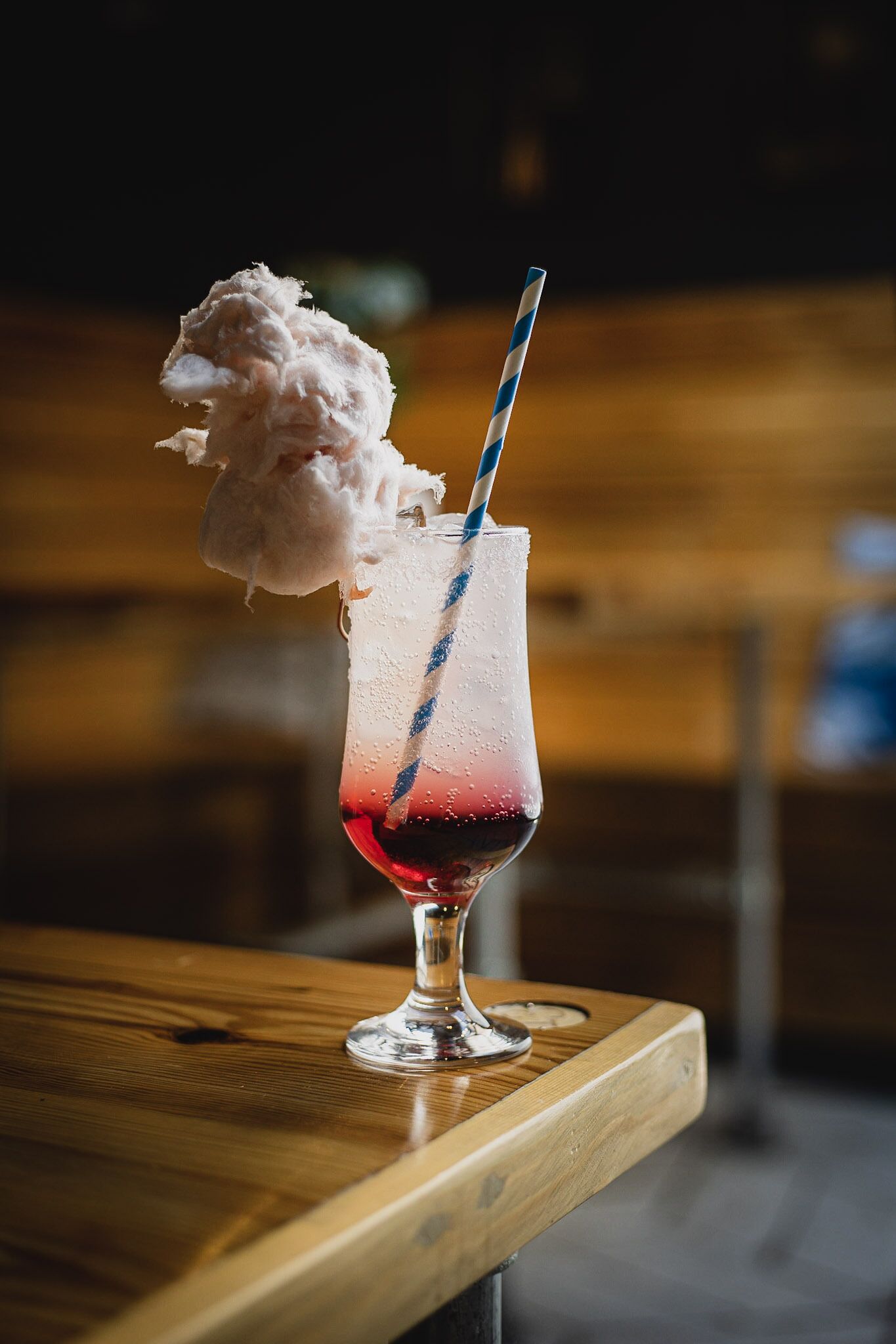 A cocktail glass with a red liquid and a blue-striped straw, topped with a scoop of ice cream.