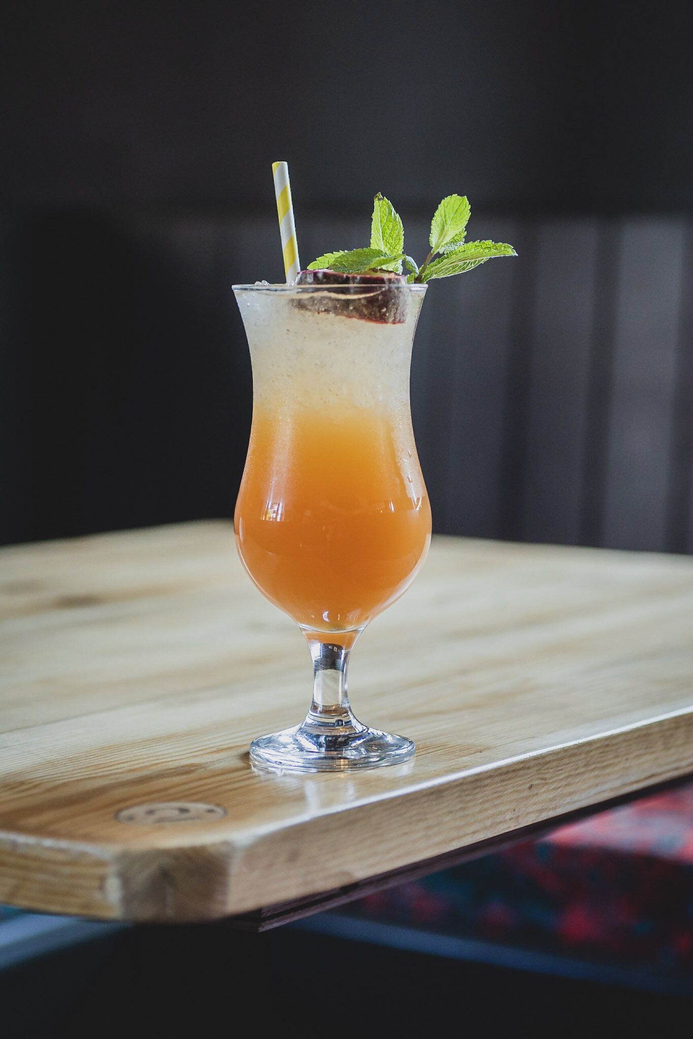 Un cocktail servi dans un grand verre, avec une paille et une feuille de menthe en guise de décoration, posé sur une surface en bois.