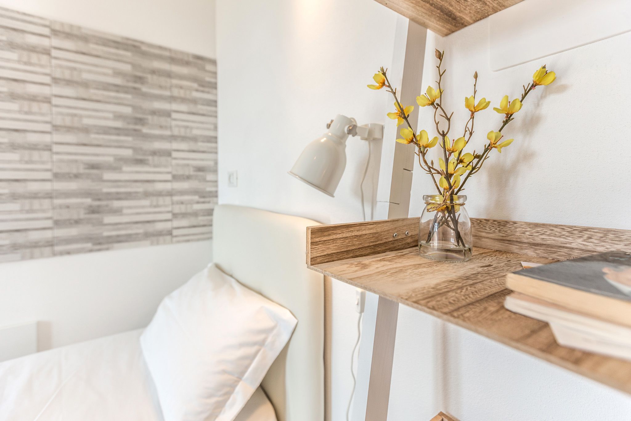 Una habitación moderna con una mesita de noche de madera, una lámpara blanca y un jarrón con flores amarillas.
