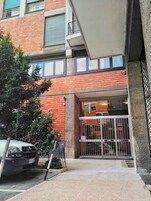 Entrada de un edificio con un camino de entrada porticado, un coche estacionado y un árbol en primer plano.