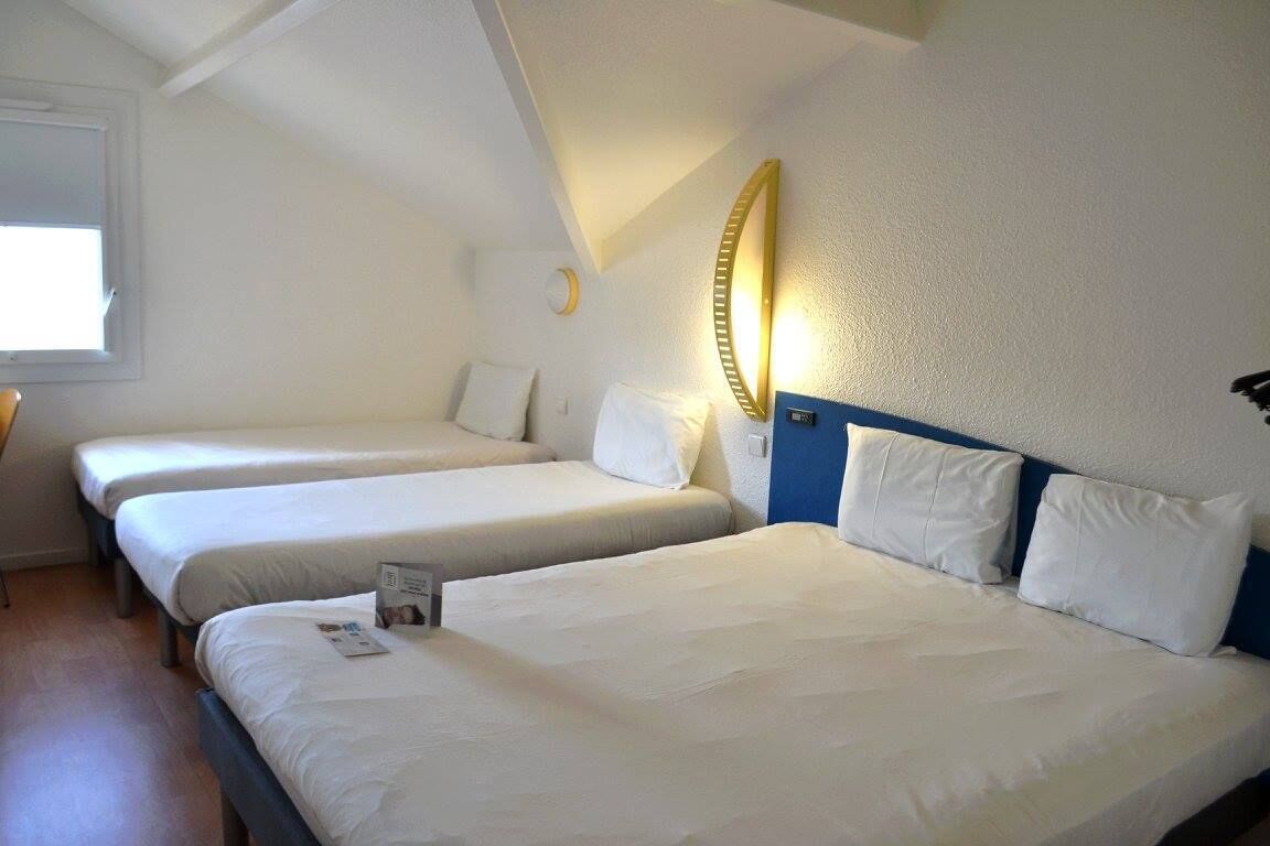 A hotel room with two single beds, a large mirror, and a small table.