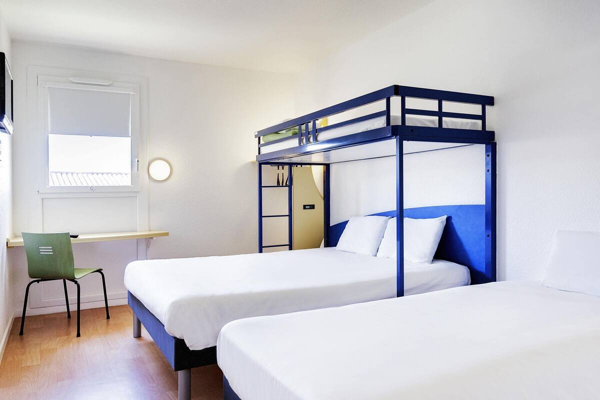 A room with two bunk beds, a desk, a chair, and a window.