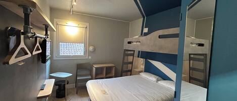 Habitación de hotel compacta con literas, un escritorio pequeño y una ventana con persianas.