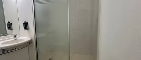 Une salle de bain avec une douche à parois de verre, un lavabo et deux distributeurs de savon.