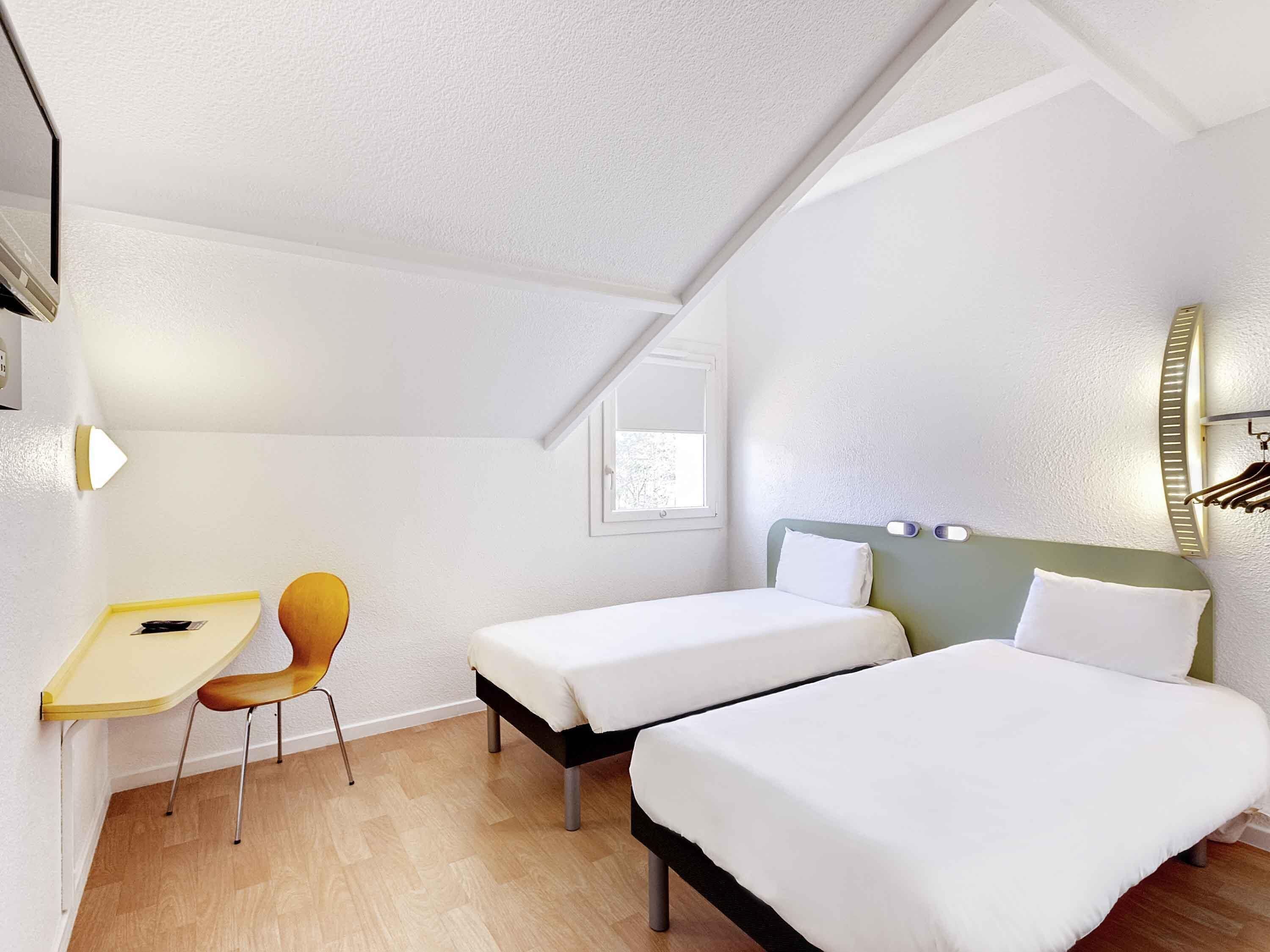 A bedroom with two beds, a desk, and a chair.