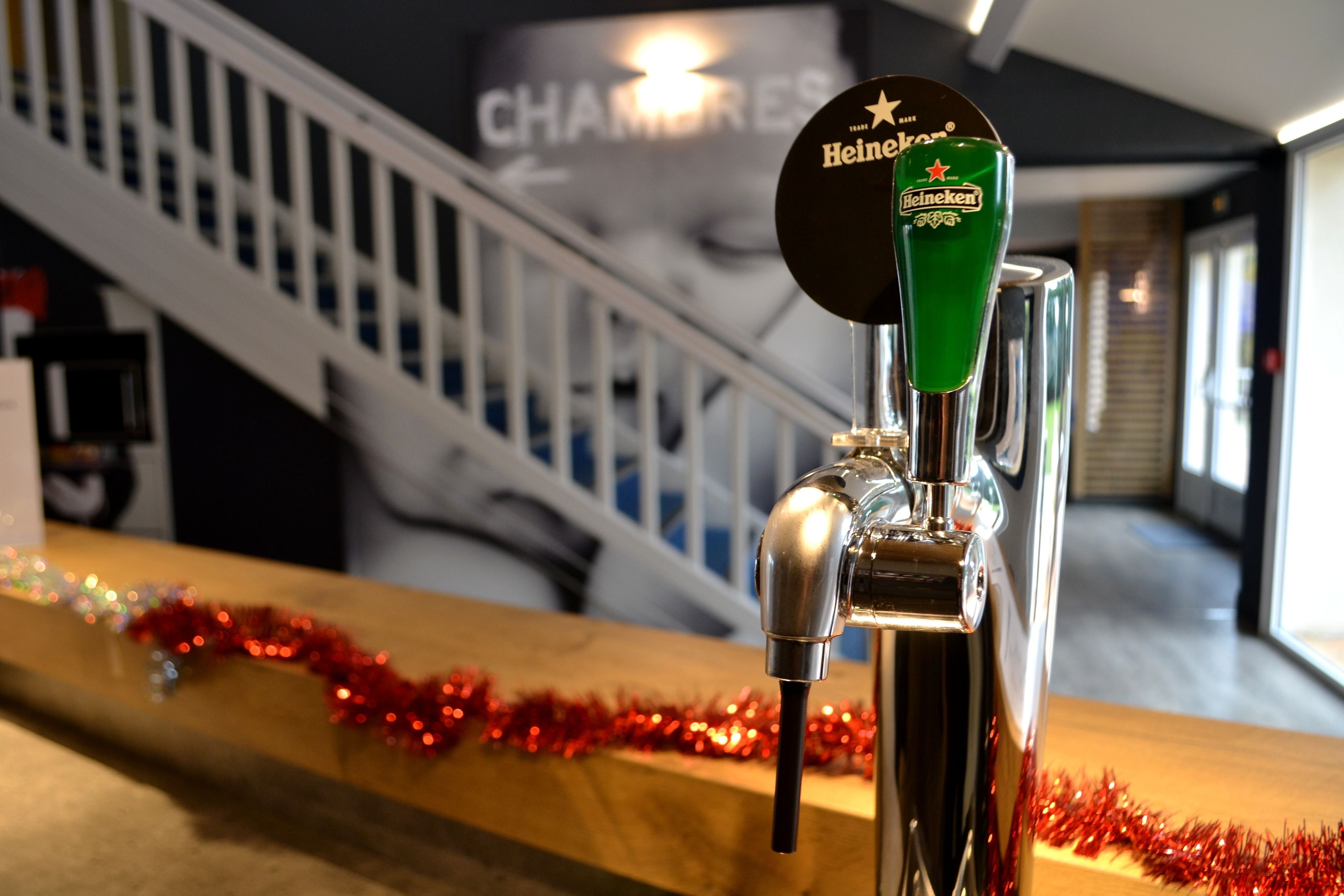 A beer tap with a green label and a star logo, a staircase in the background, and red tinsel on a counter.