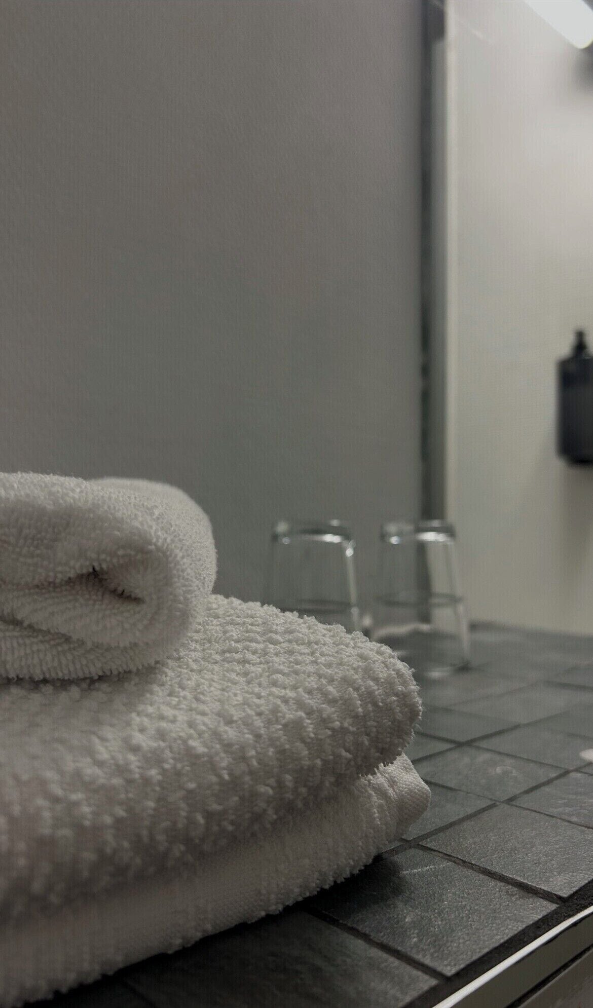 A bathroom with a towel stacked on a dark countertop. There are two clear glass bottles on the counter.