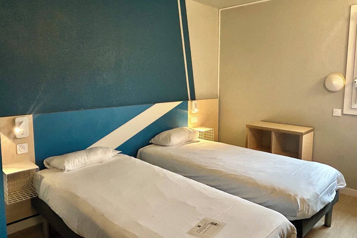 A room with two beds, a blue and white striped headboard, bedside lamps, and a small wooden nightstand.