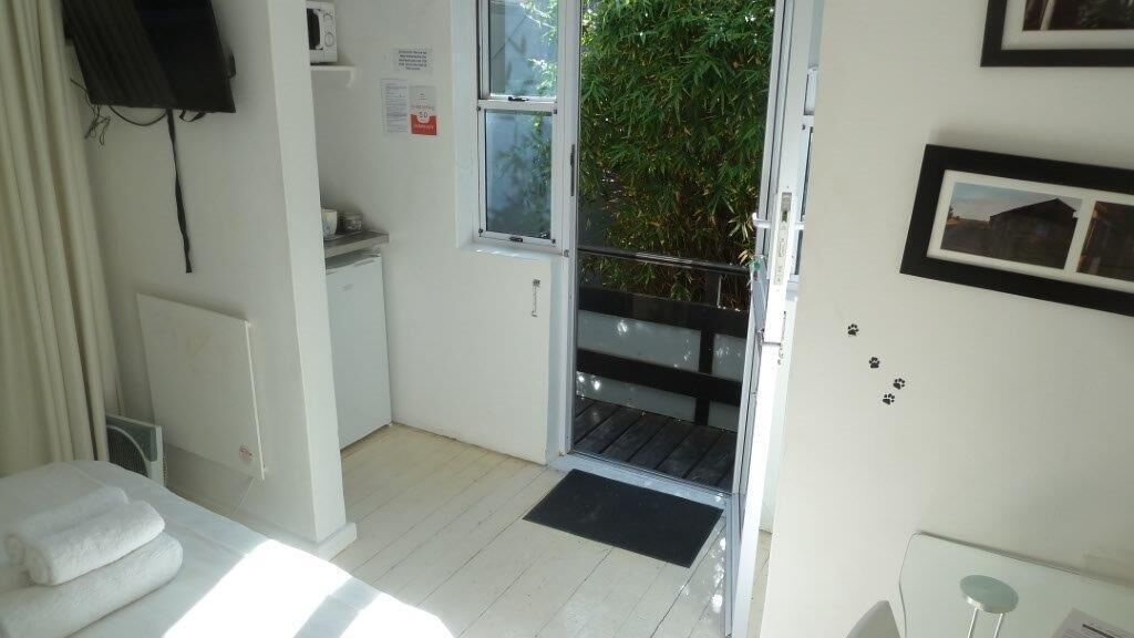Ein Zimmer mit einem Bett, einem kleinen Tisch, einem Fenster, einer Tür und Blick auf Grünfläche.