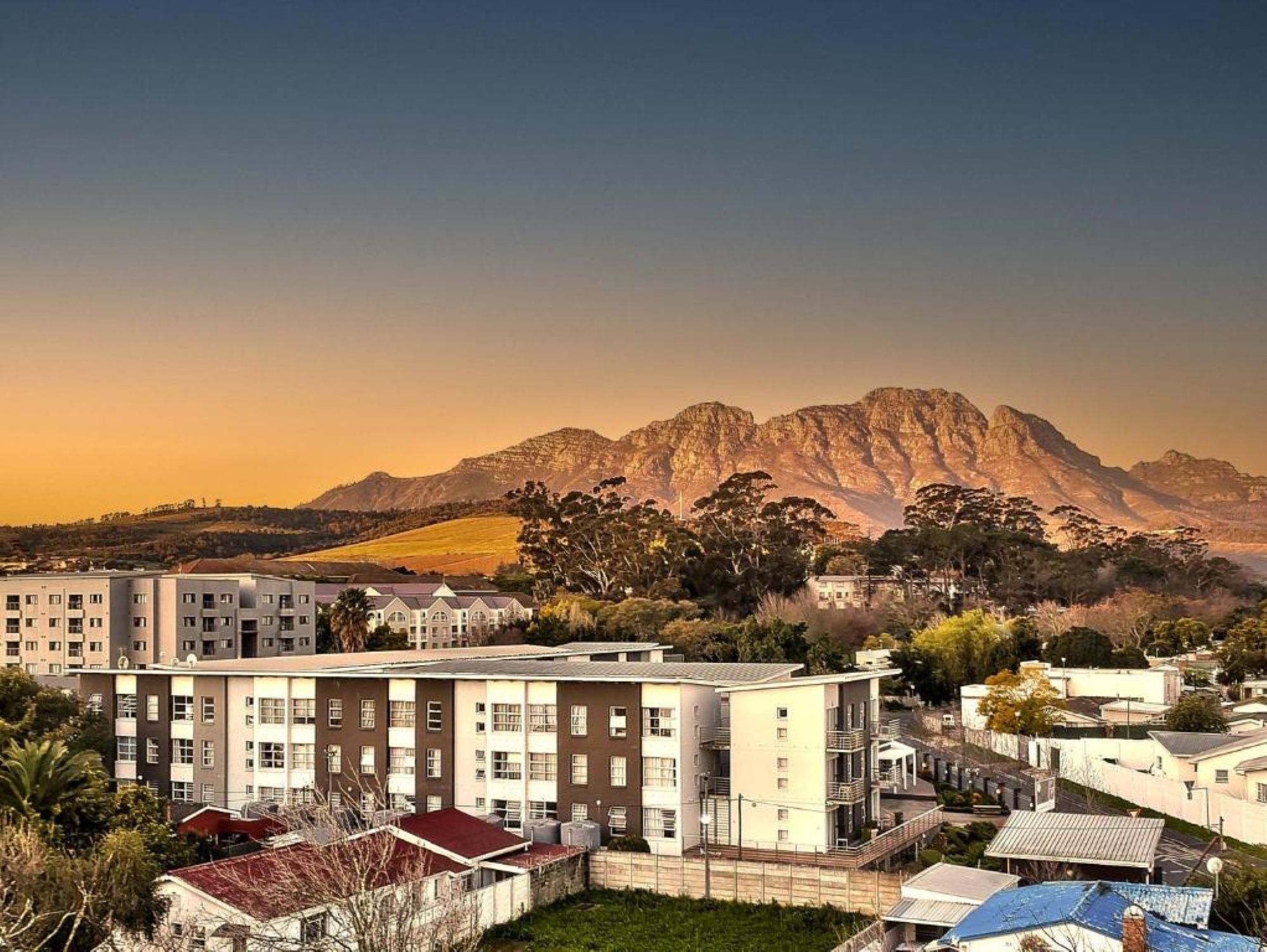 A residential area with apartment buildings, a mountain in the background, and a clear sky.