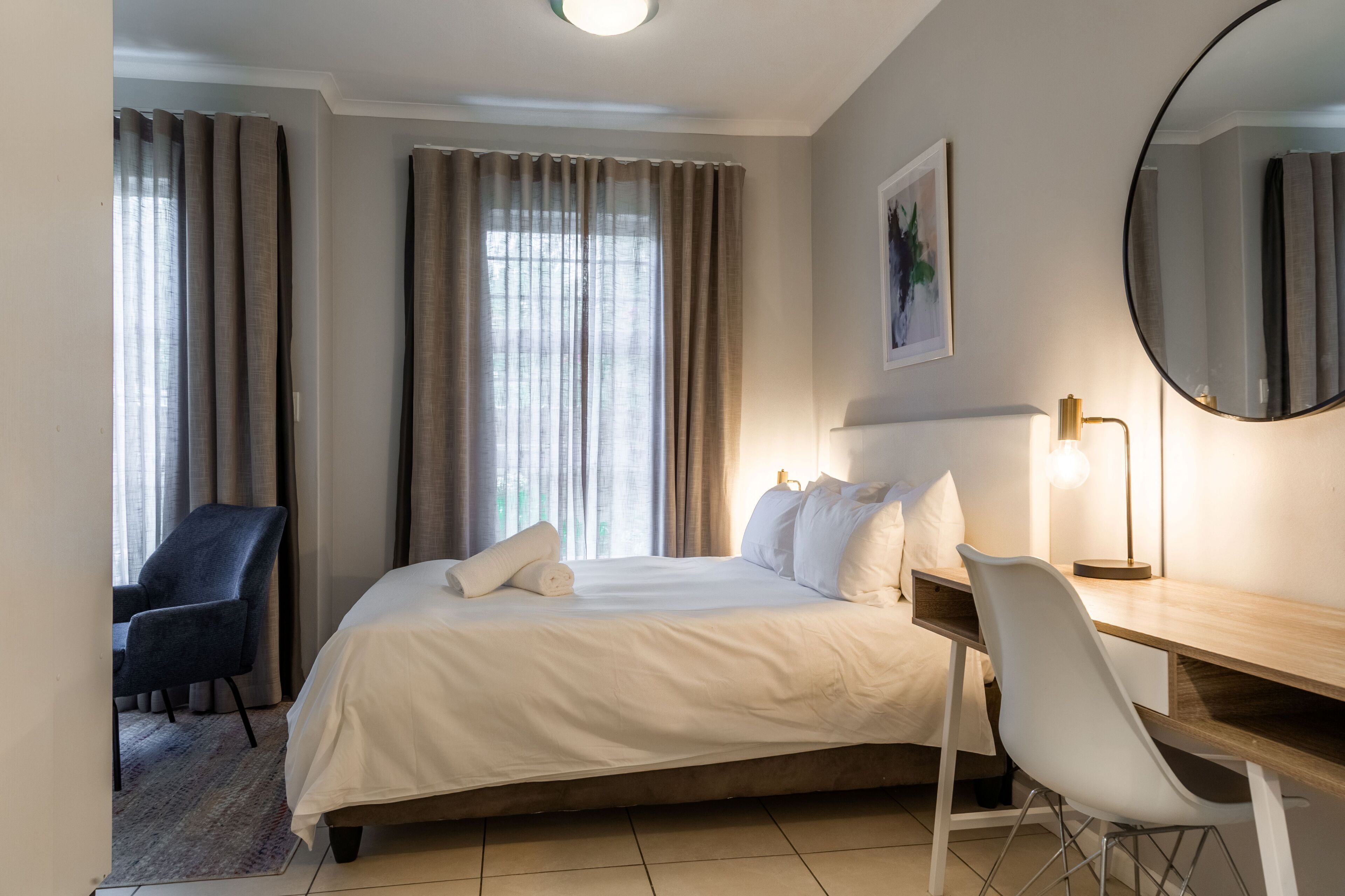 Habitación de hotel con cama, escritorio, silla, lámpara de escritorio y un espejo grande.