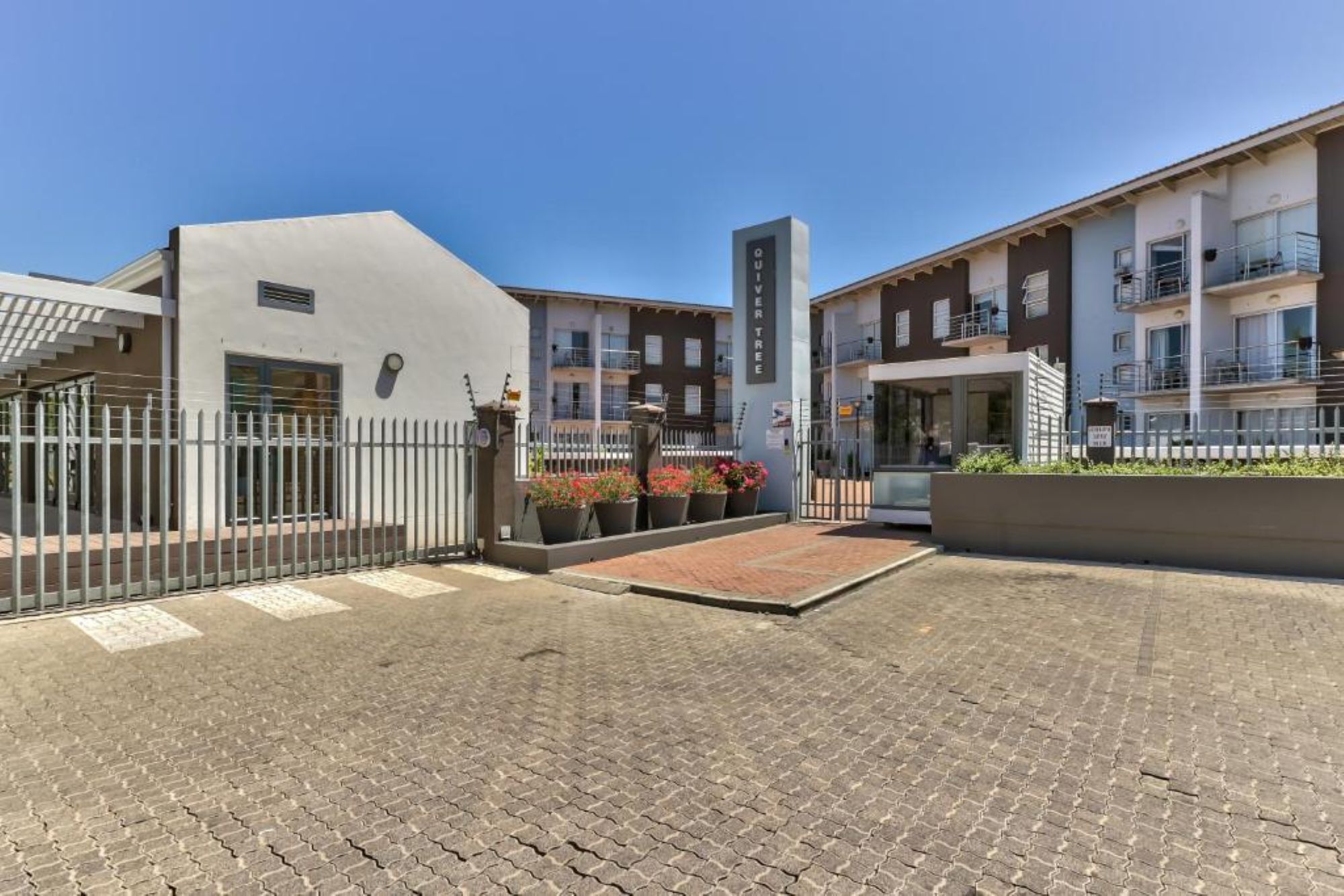 A building with a gated entrance, a vertical sign, and a paved courtyard.