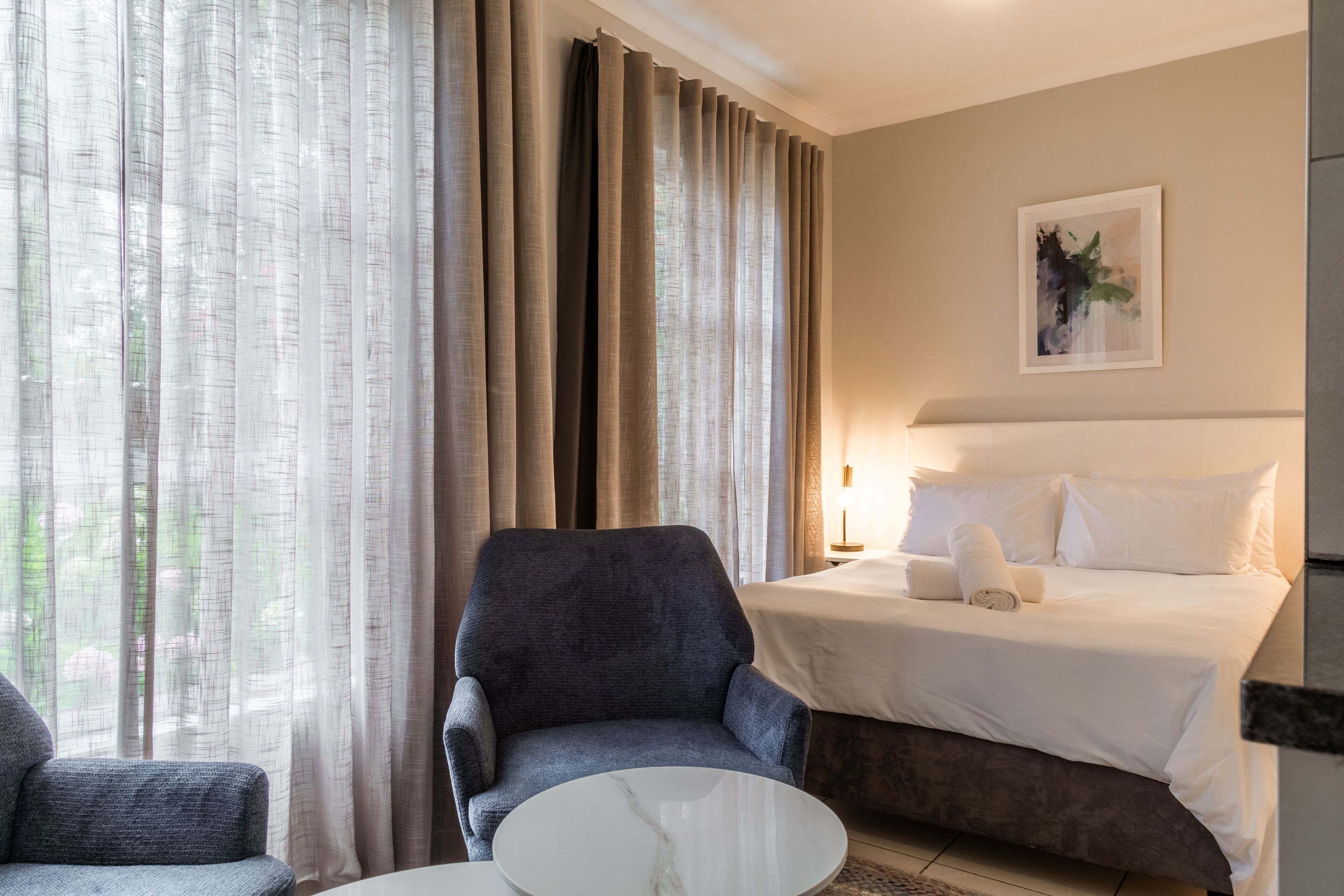 A hotel room with a bed, a chair, a round table, and curtains.