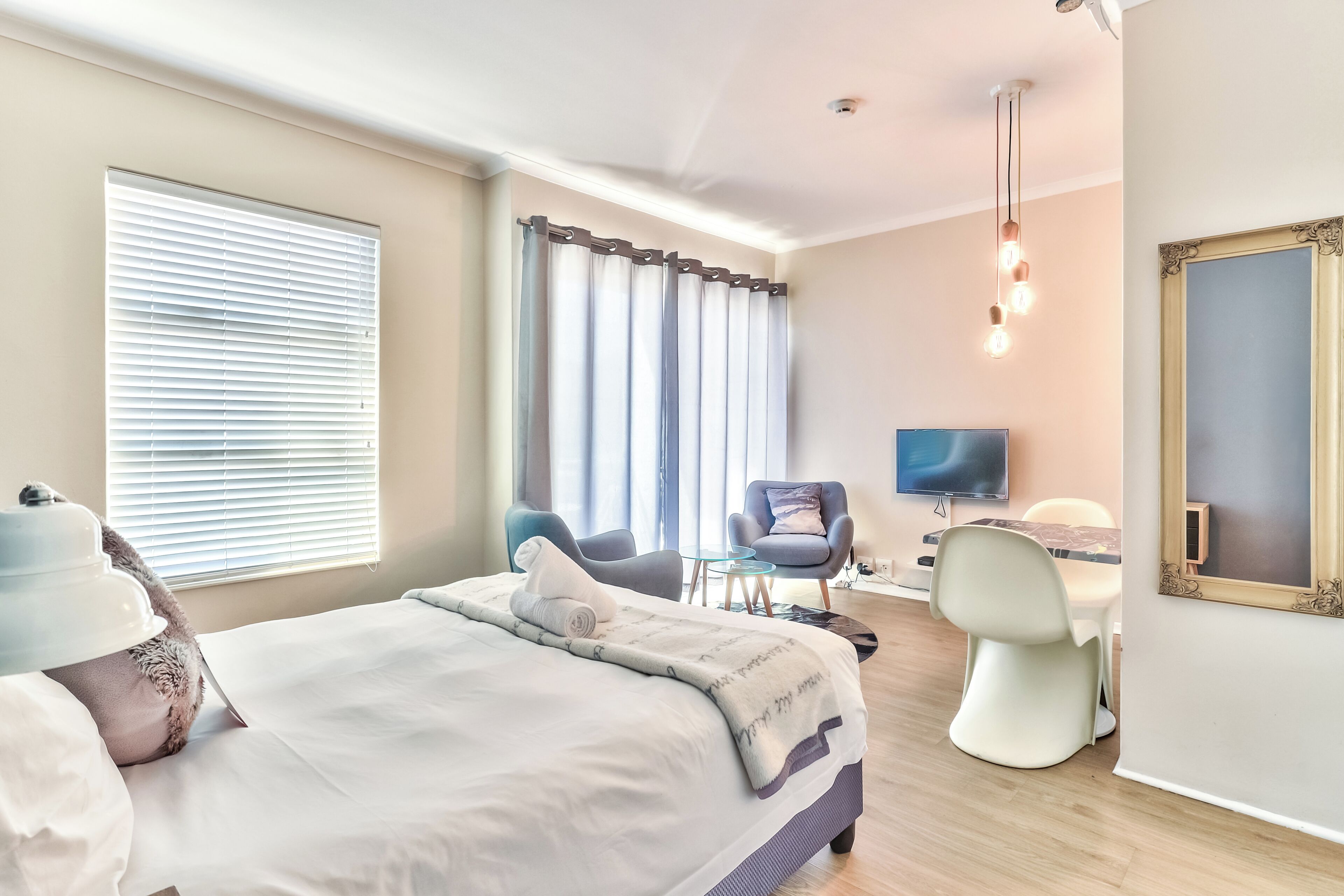 A modern hotel room with a large bed, a desk with a chair, a television, and a large mirror.