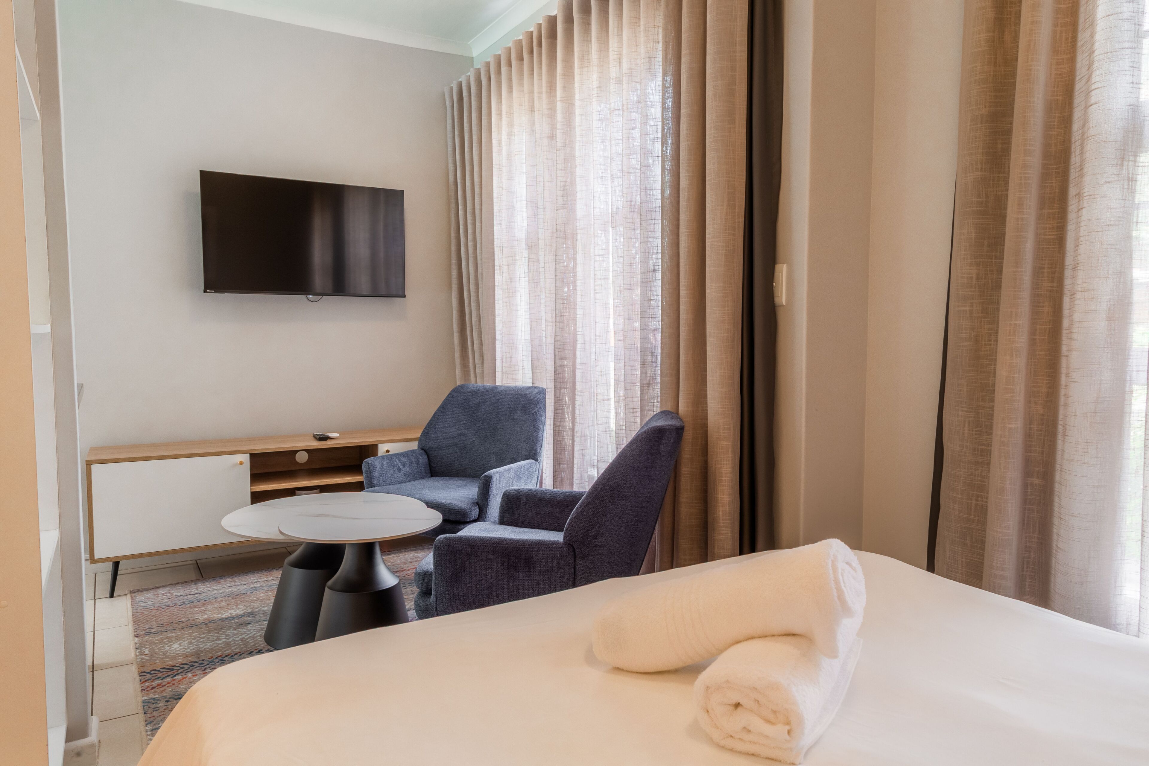 Een hotelkamer met een bed, een bureau, twee stoelen, een televisie en een raam met gordijnen.