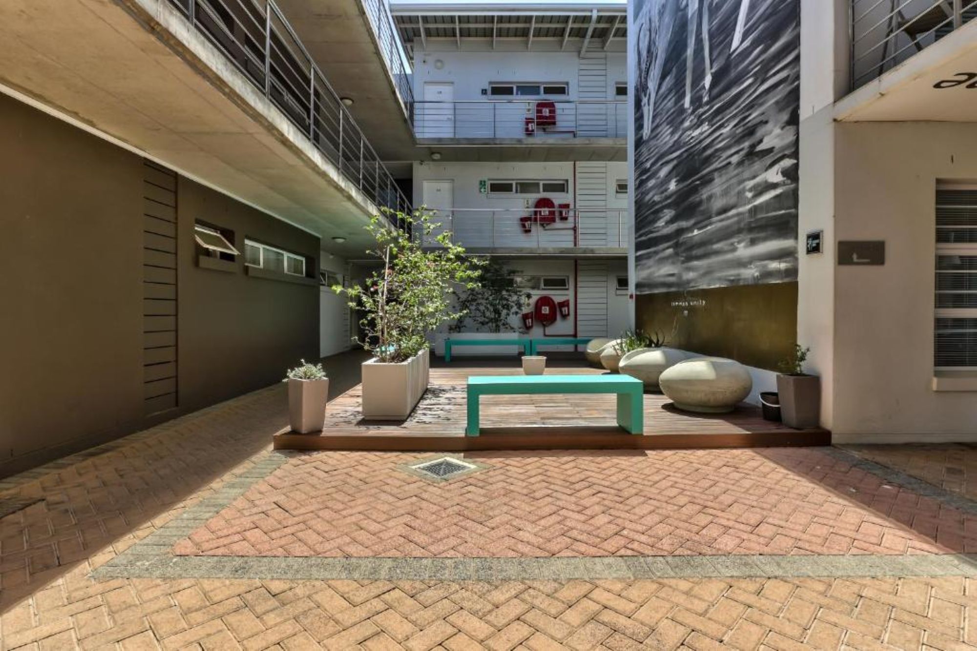 A courtyard with a bench, potted plants, and a building with fire safety equipment.