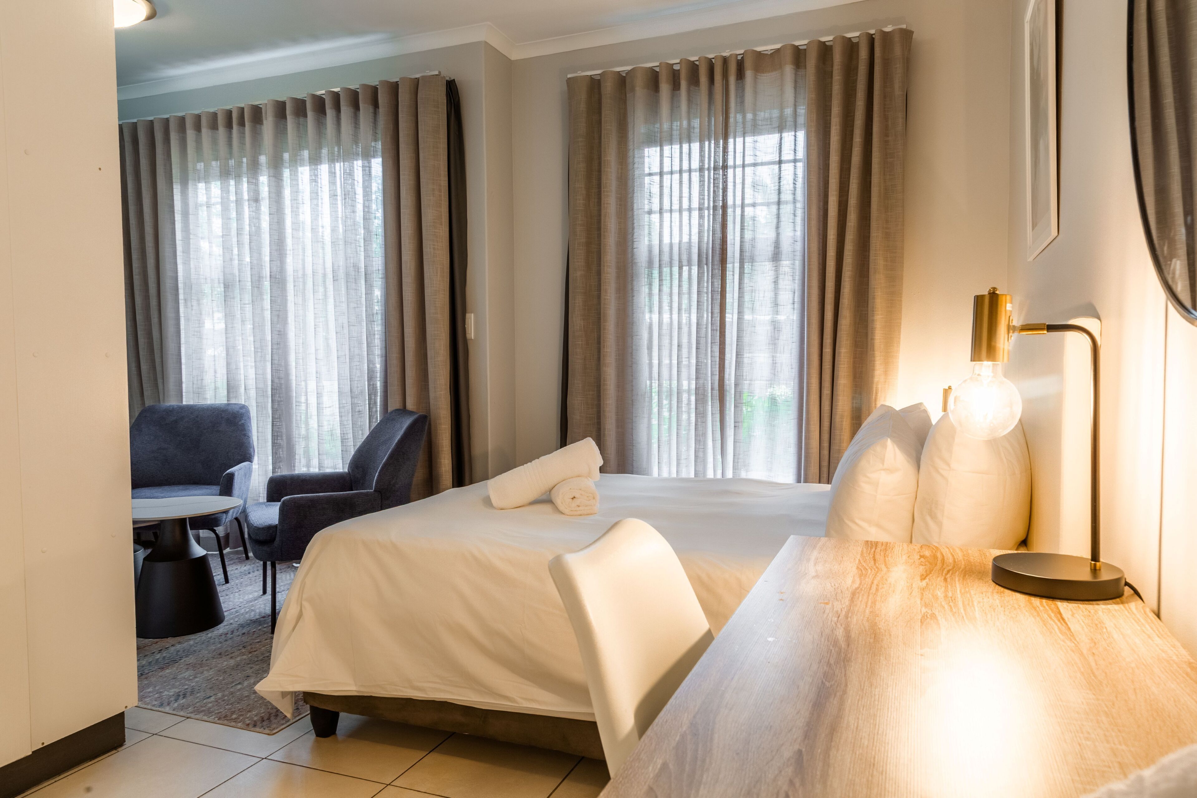 Una habitación de hotel con cama, escritorio, silla y cortinas.
