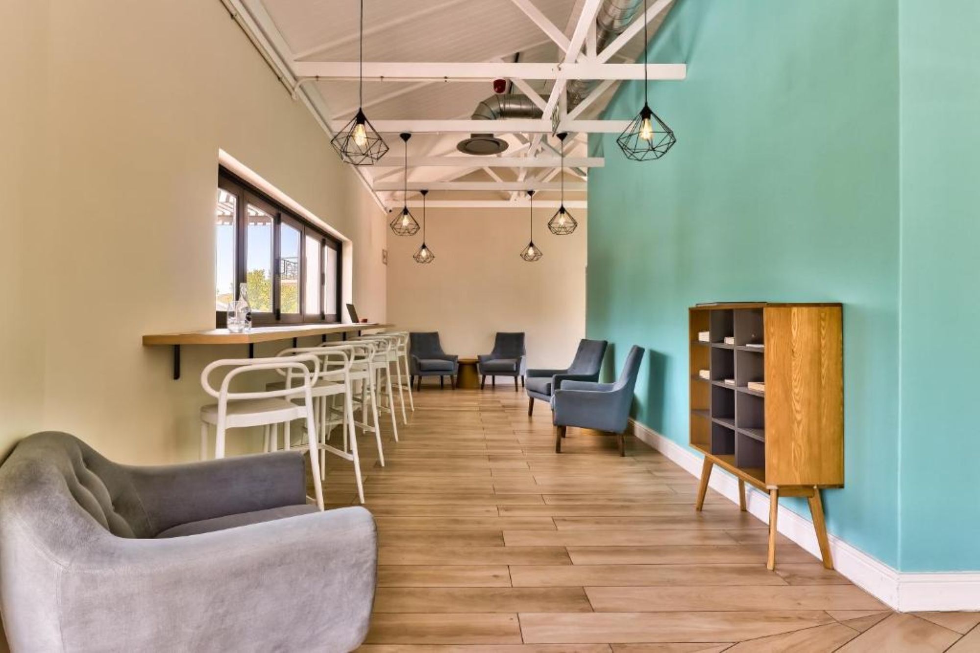 A modern interior with a wooden floor, white chairs, a teal wall, and pendant lights.