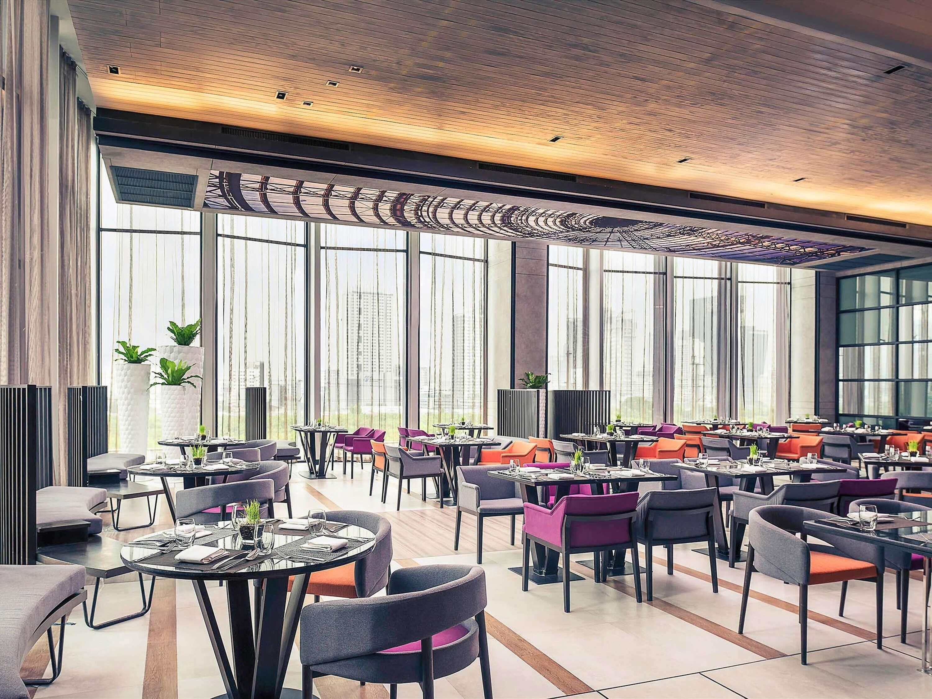 A modern dining area with multiple tables and chairs, large windows, and a patterned ceiling.