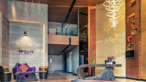 A modern hotel lobby with a reception desk, seating area, and a staircase leading to an upper level. - Mercure Bangkok Makkasan (Bangkok)