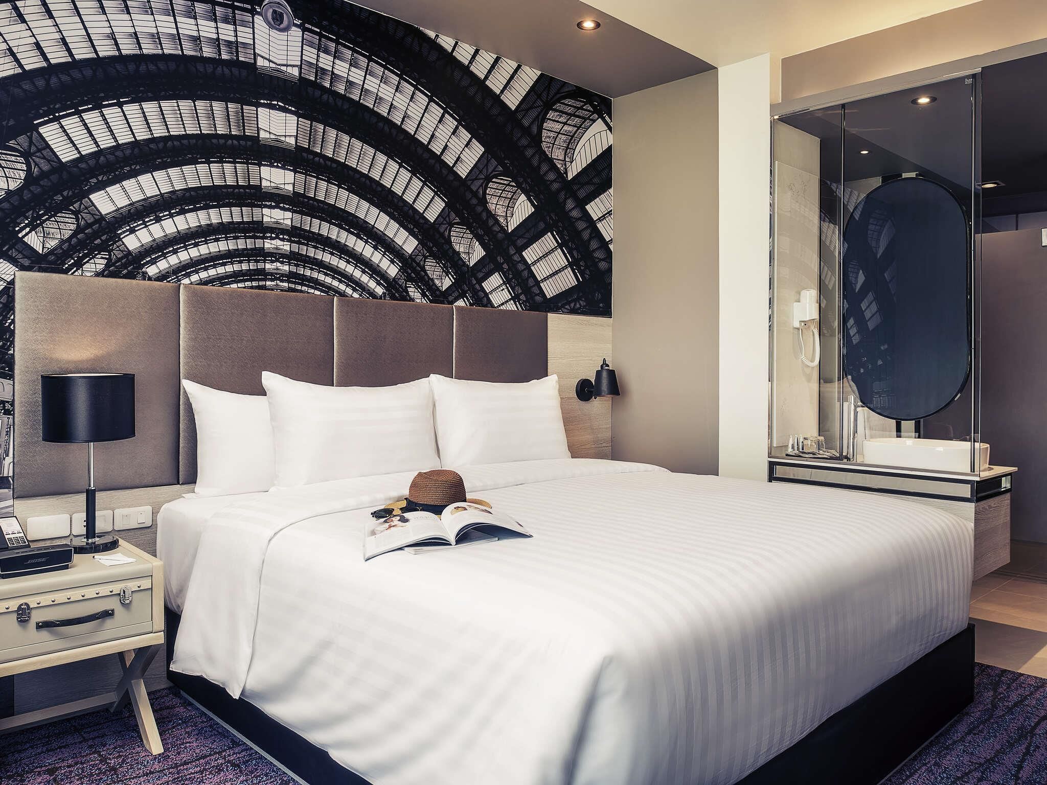 Een hotelkamer met een groot bed, een nachtkastje met een lamp, een bijzettafeltje met een telefoon en een grote spiegel.