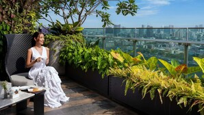 A woman sitting on a balcony with a city view, surrounded by lush plants and a modern interior. - Mercure Bangkok Makkasan (Bangkok)