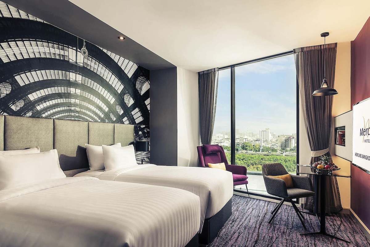 Een hotelkamer met een groot bed, een stoel, een bureau en uitzicht op de stad.