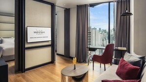 A modern hotel room with a city view, a round coffee table, a sofa, and a red chair. - Mercure Bangkok Makkasan (Bangkok)