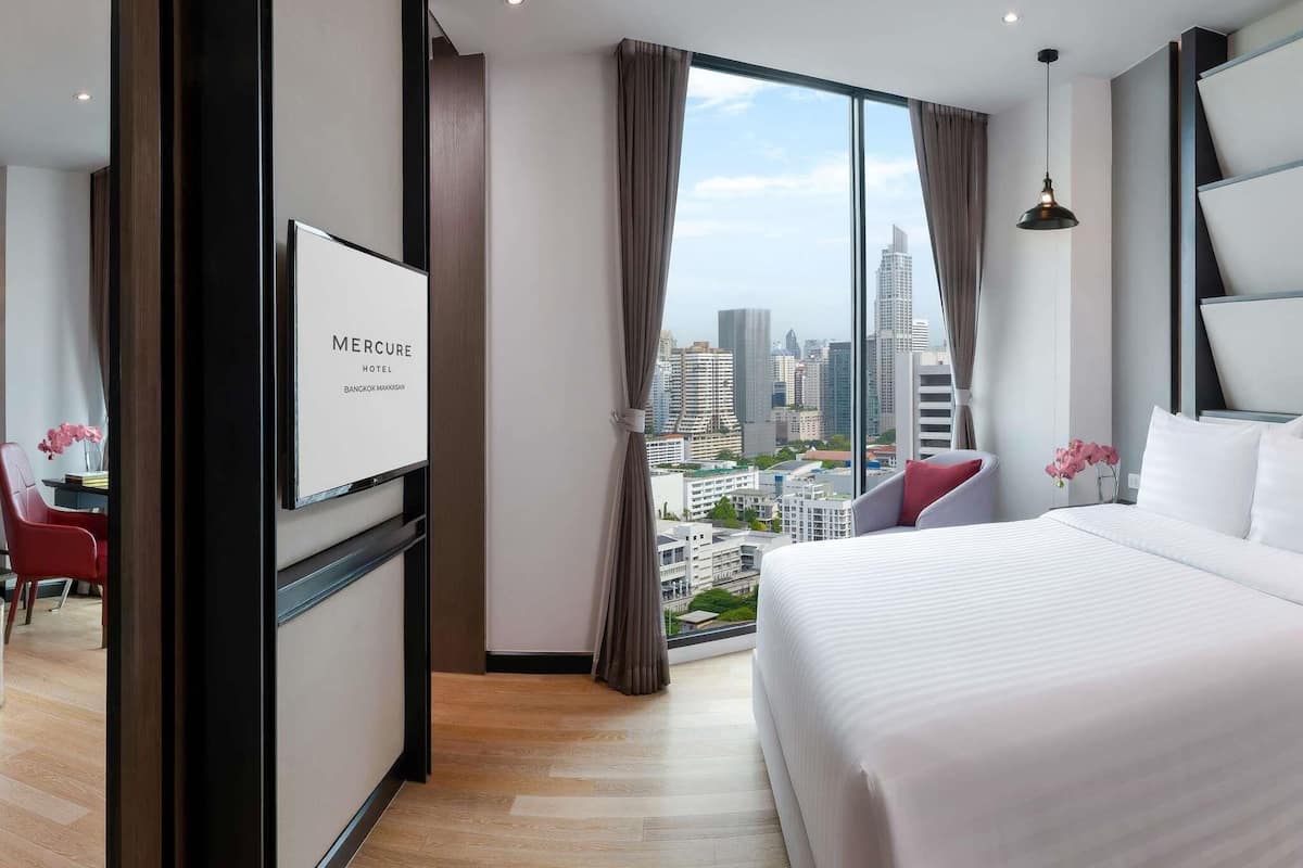 A hotel room with a large bed, a desk, and a view of a cityscape.