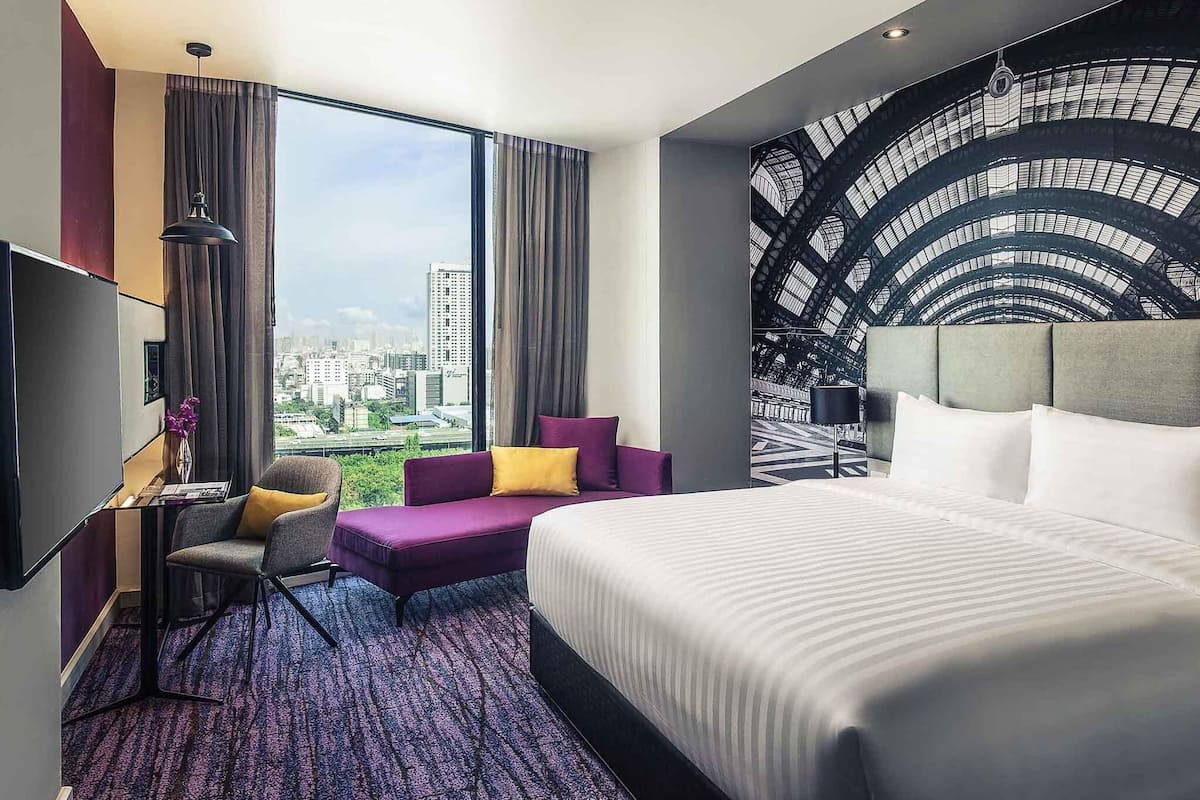 A hotel room with a large bed, a seating area with a view of the city, and a wall with a geometric pattern.