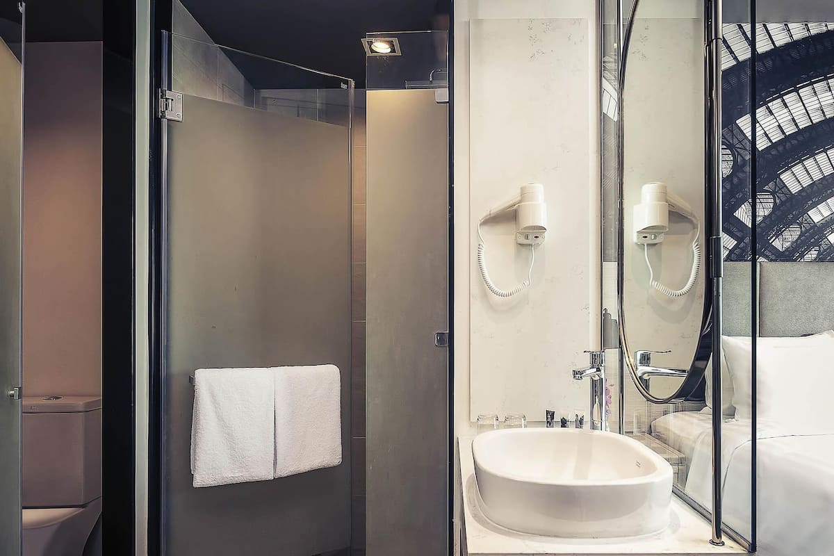 A modern bathroom with a glass shower enclosure, a white sink, and a mirror with a towel hanging on the wall.