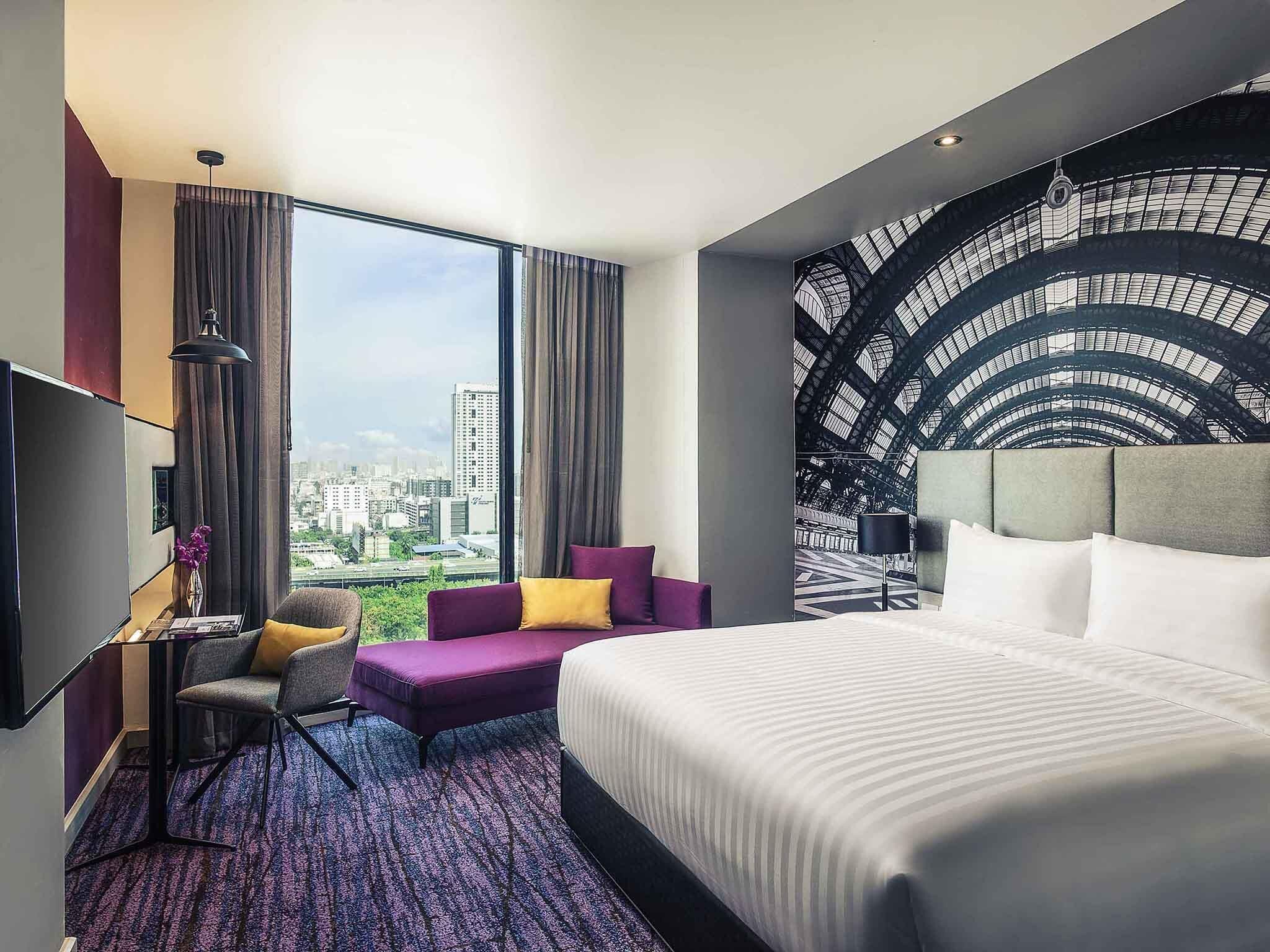 Hotelkamer met een groot bed, een zithoek met uitzicht over de stad, en een muur met een geometrisch patroon.