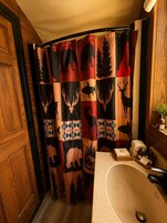 Un baño con cortina de ducha estampada con motivos de animales, una puerta de madera y un lavabo con artículos de aseo.