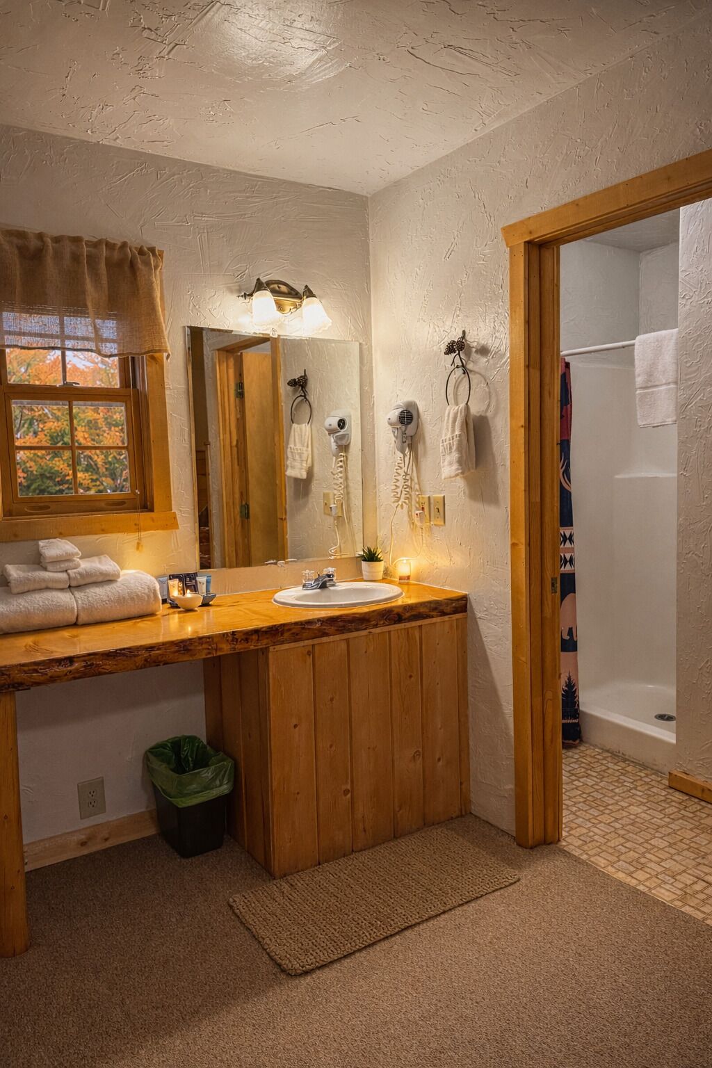 A bathroom with a wooden vanity, a sink, a mirror, a towel rack, and a shower area.