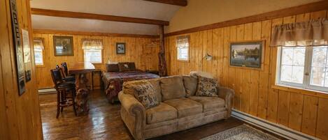 A cozy room with wooden walls and a ceiling fan, a bed with a quilt, a sofa, and a dining table with chairs.