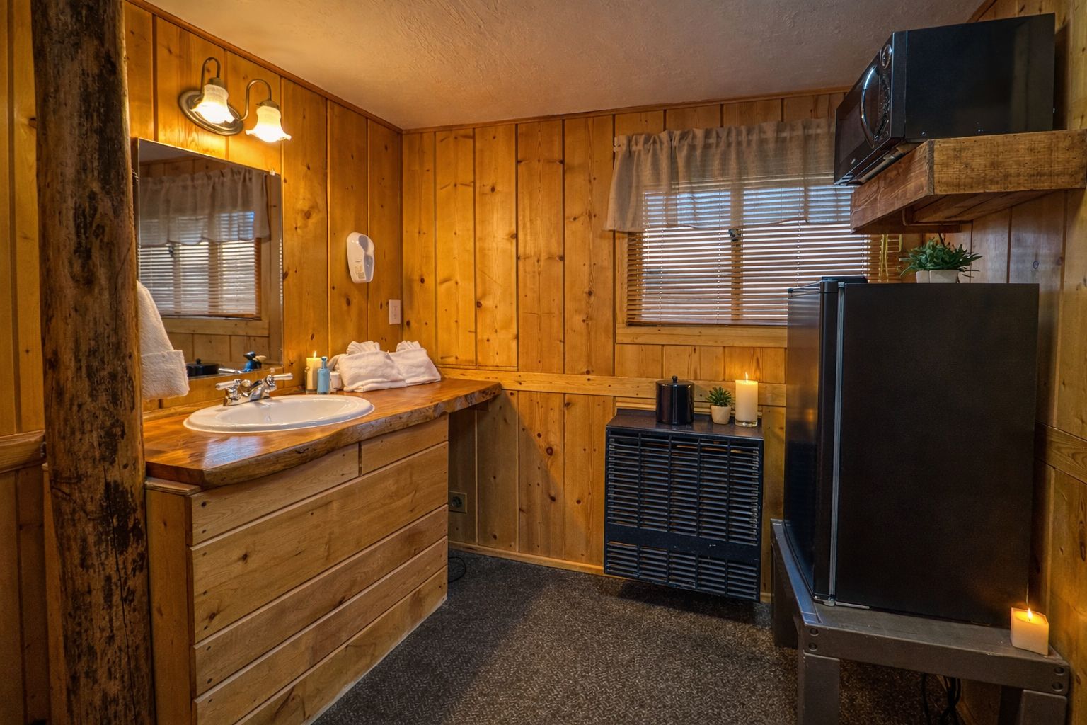 Baño de cabaña de madera con lavamanos, espejo, toallero y un microondas en un estante.