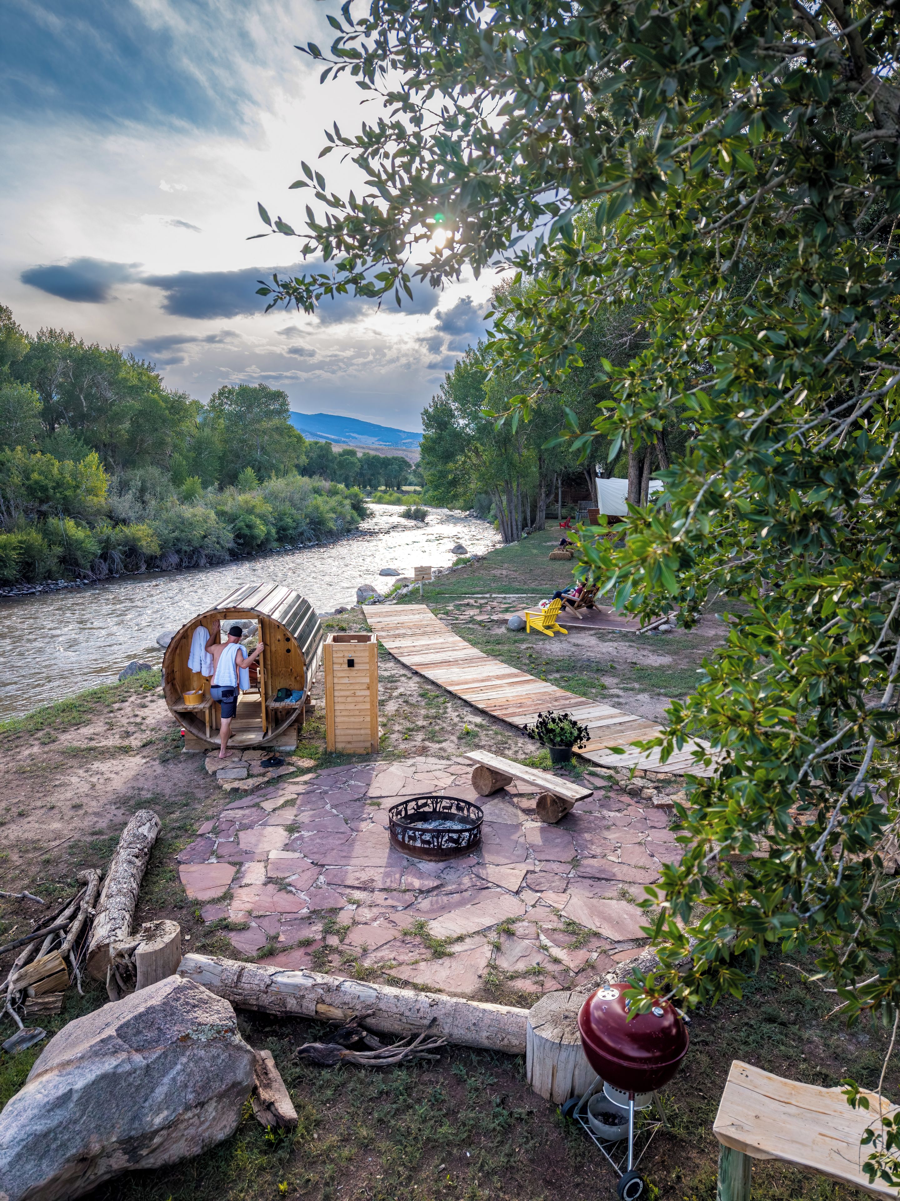 A rustic outdoor setting with a wooden barrel structure, a fire pit, and a barbecue grill.