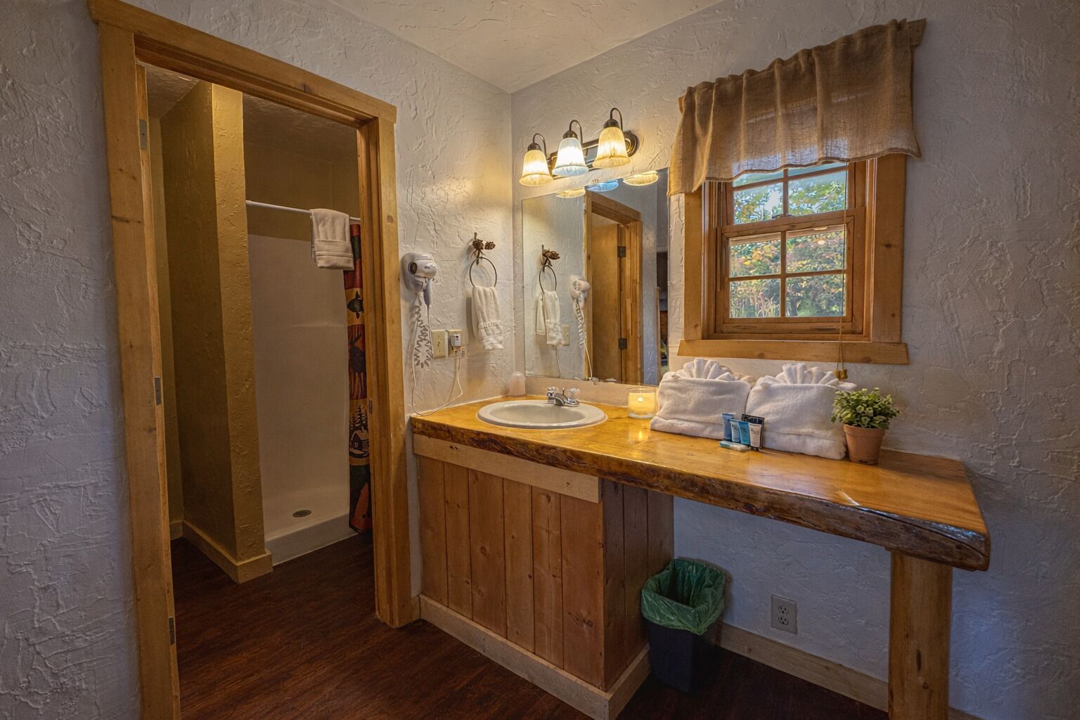 A bathroom with a wooden vanity, a sink, a mirror, and a window with curtains.